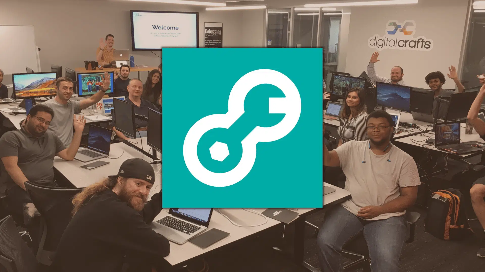 DigitalCrafts classroom with students at computers, smiling and raising hands during a coding session in a modern training space