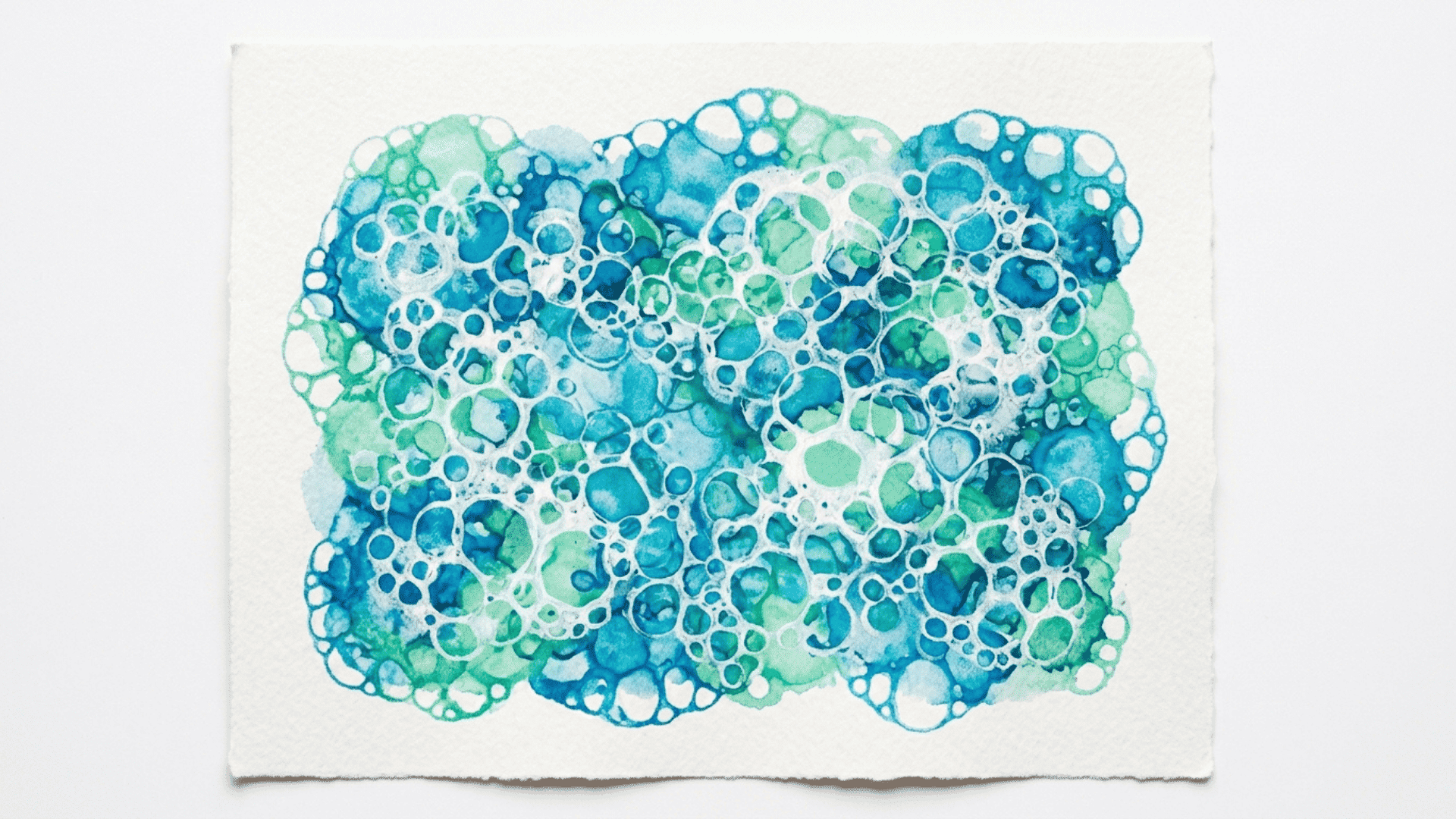 bubble paint sea foam art showing layered circular bubble prints in blue green and white paint on white paper for kids