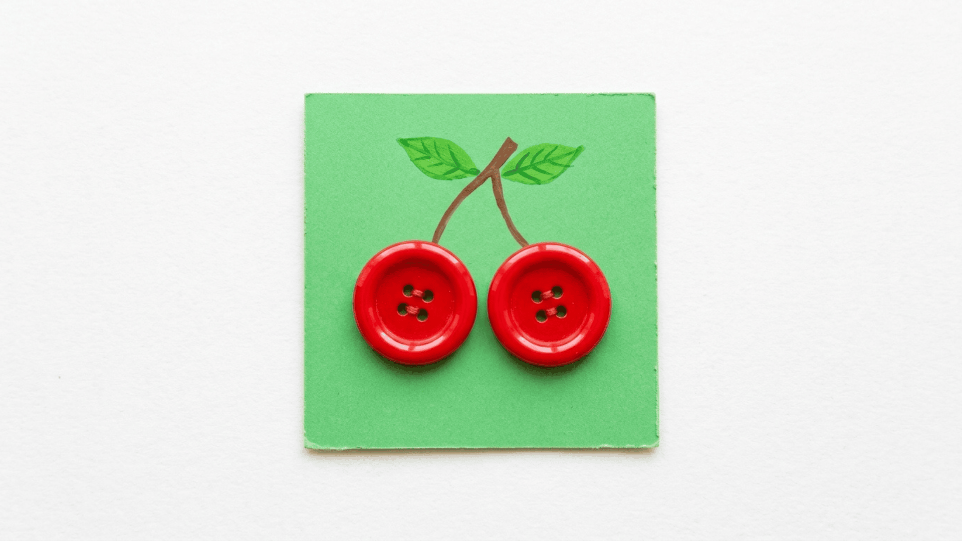 button cherry craft showing two shiny red buttons connected by brown painted stems with small green leaves on green cardstock