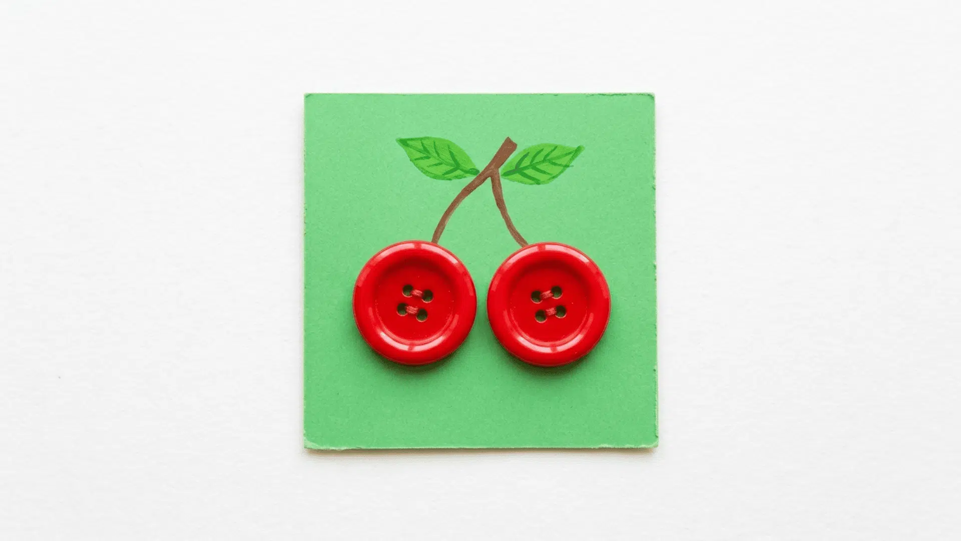 button cherry craft showing two shiny red buttons connected by brown painted stems with small green leaves on green cardstock