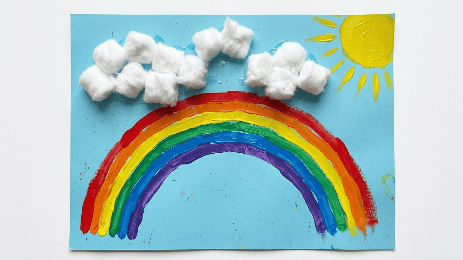 cotton ball cloud and rainbow scene showing white cotton clouds a painted rainbow arching below and yellow sun rays on paper