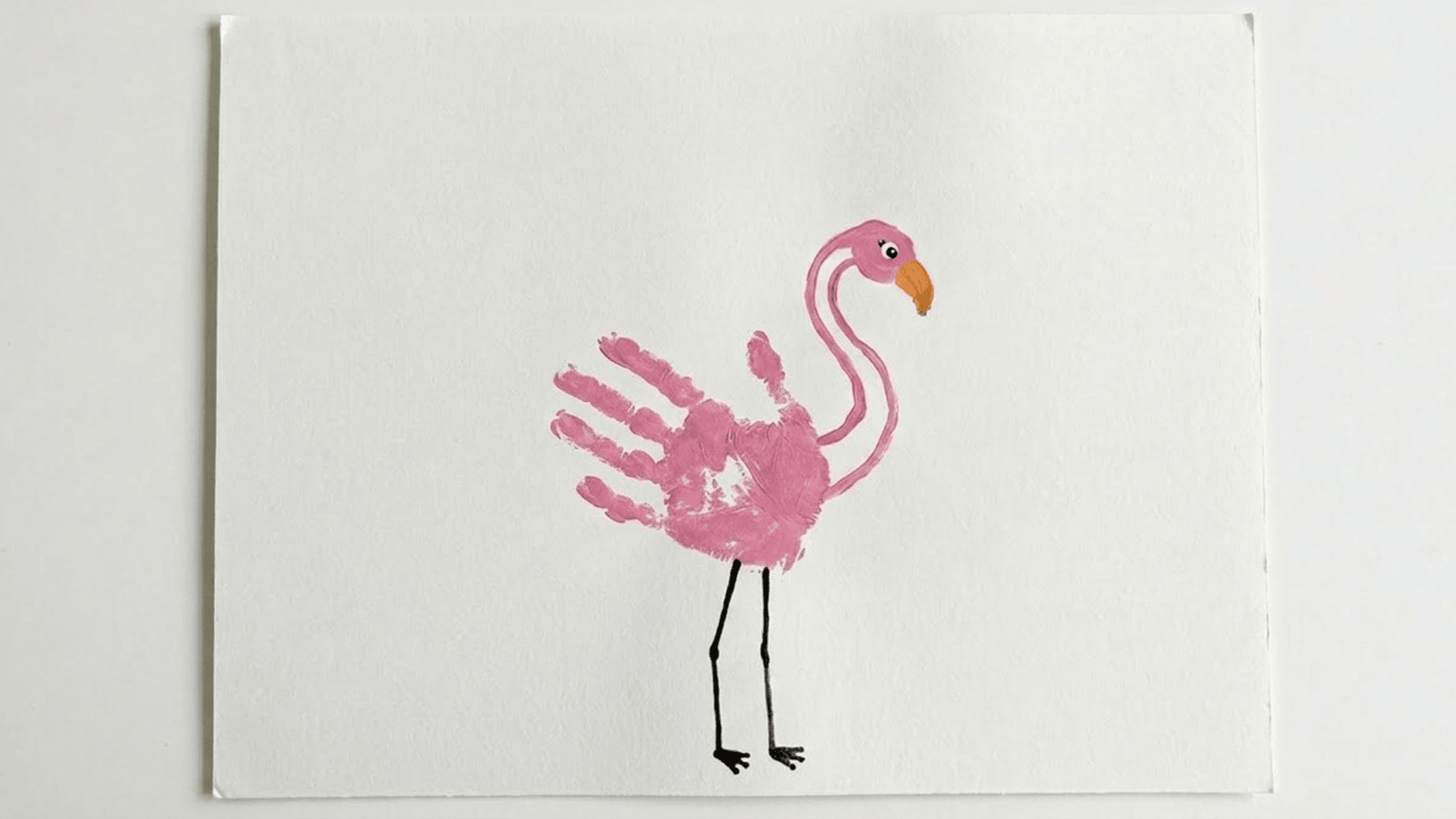 handprint flamingo painting showing a pink painted handprint forming the bird body with a curved neck and stick legs on paper