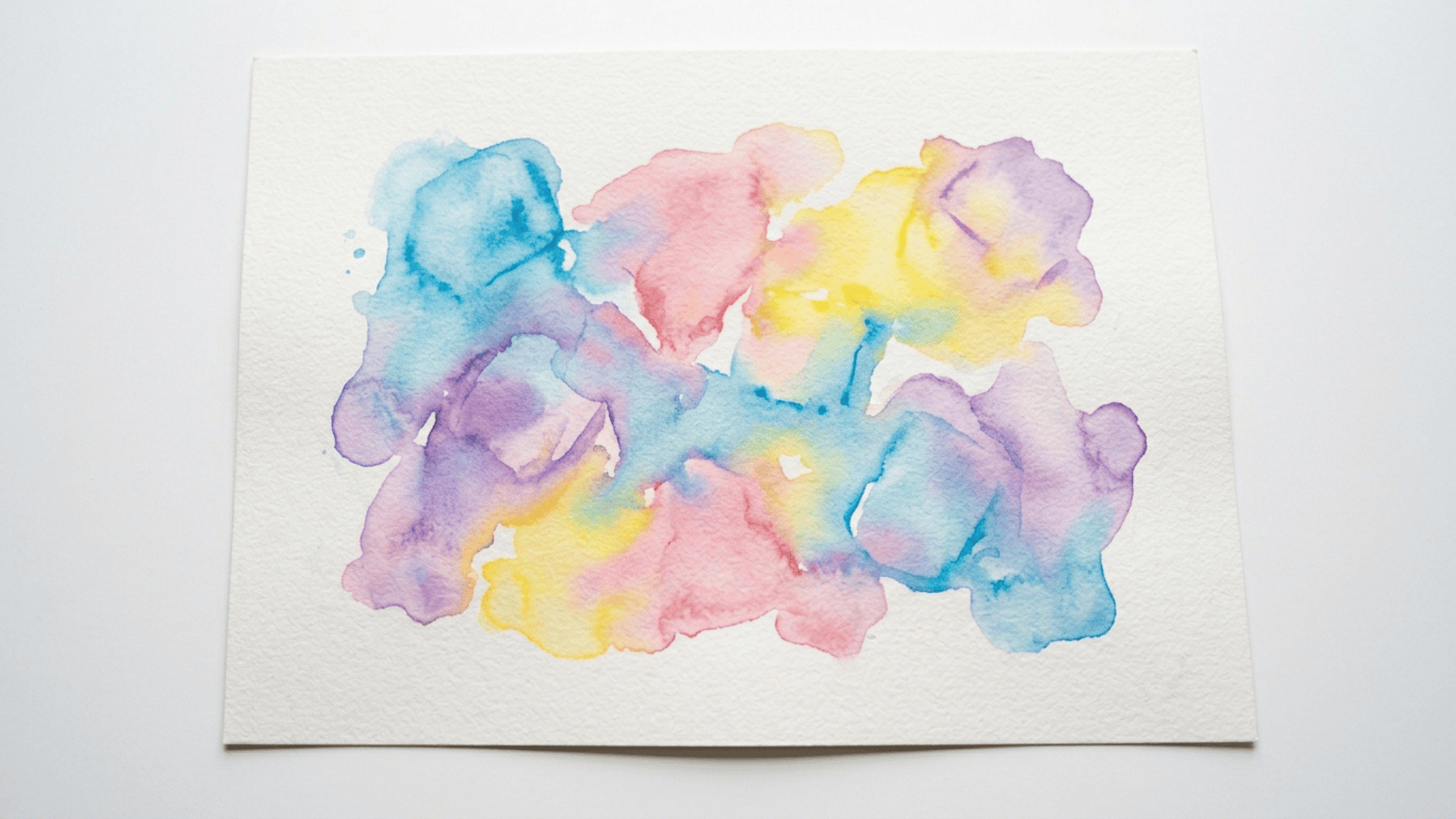 ice cube watercolor painting showing soft blended puddles of blue pink yellow and purple spreading across white paper