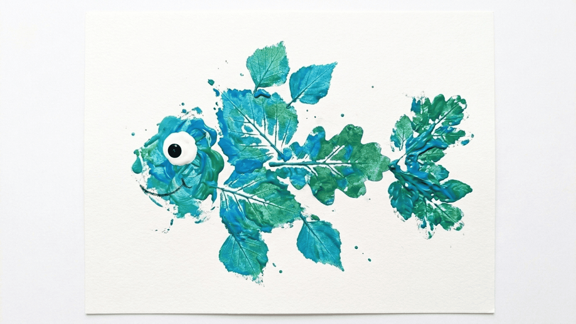 leaf print fish painting showing a fish shape made from a pressed leaf in blue and green paint with a small eye on white paper