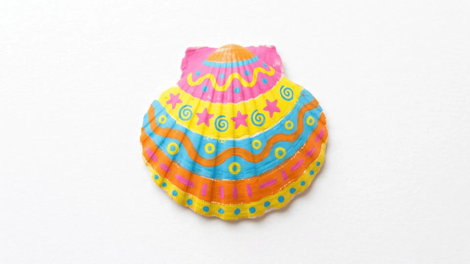 painted seashell art showing a smooth shell decorated with bright pink yellow blue and orange stripes on white background