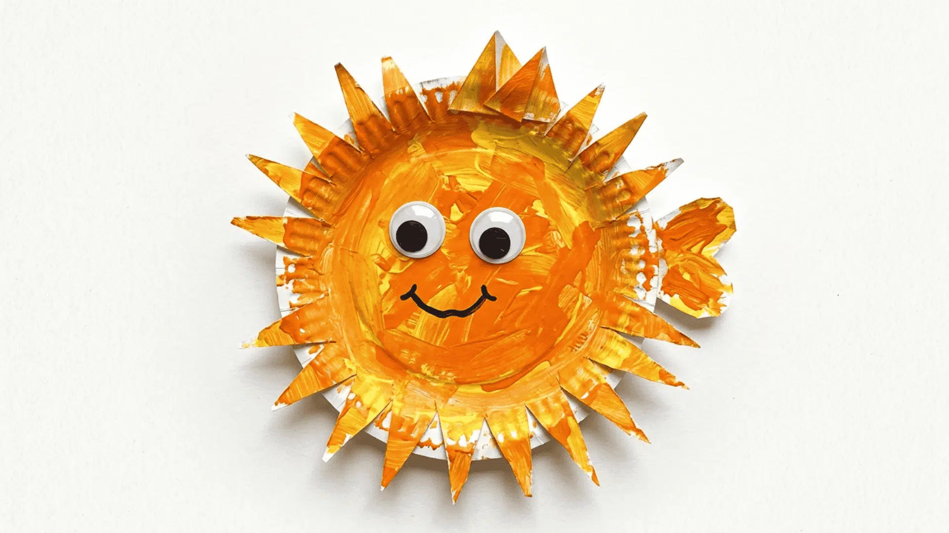 paper plate puffer fish craft with spiky folded fins googly eyes and bright orange yellow paint on white background