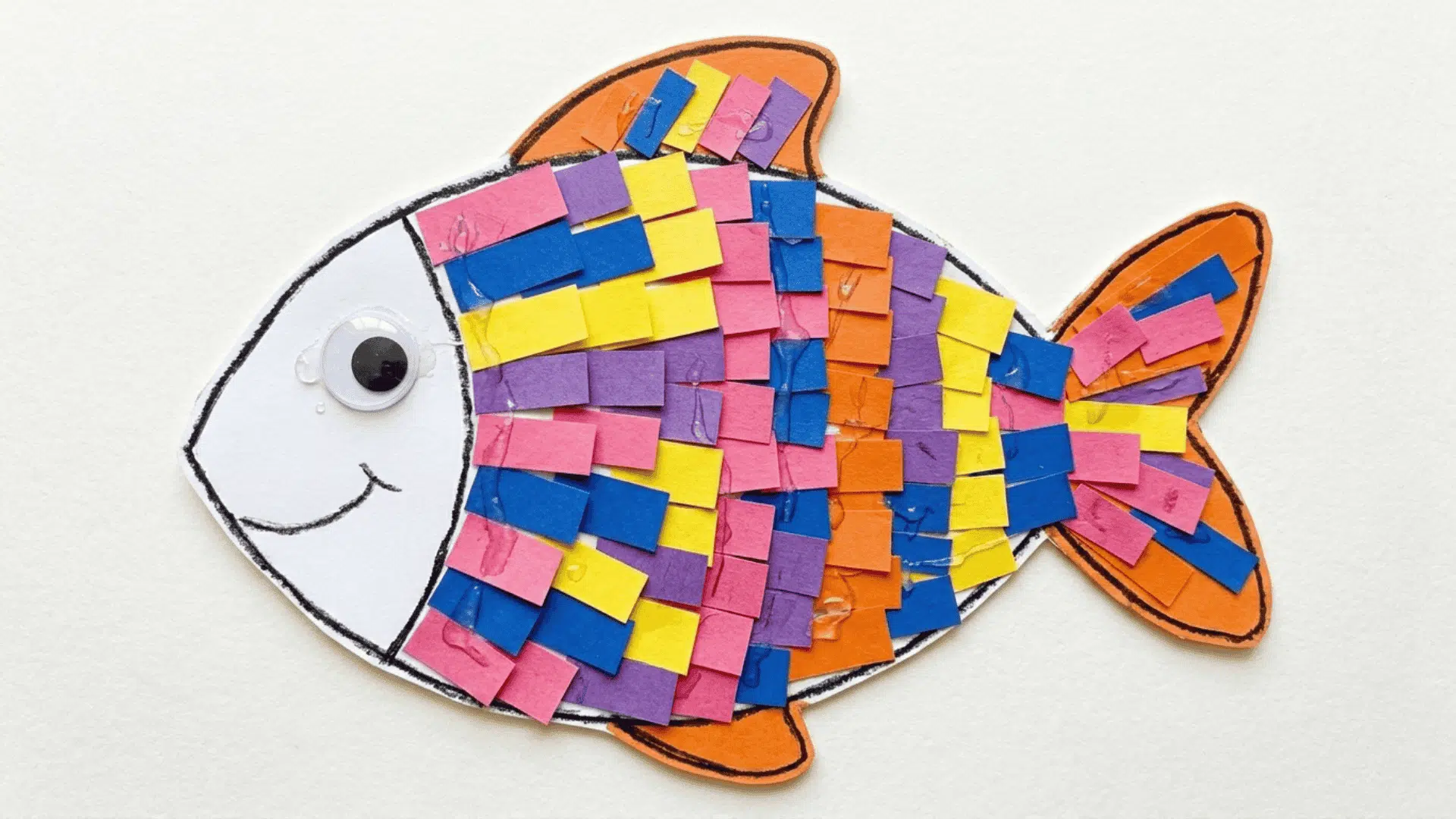 paper strip rainbow fish craft showing a fish outline filled with overlapping colorful paper strips in a scale pattern on white