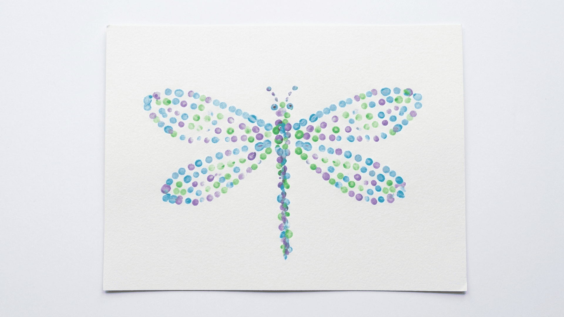 q tip dragonfly art showing a dragonfly shape built from small painted dots in blue purple and green on white paper