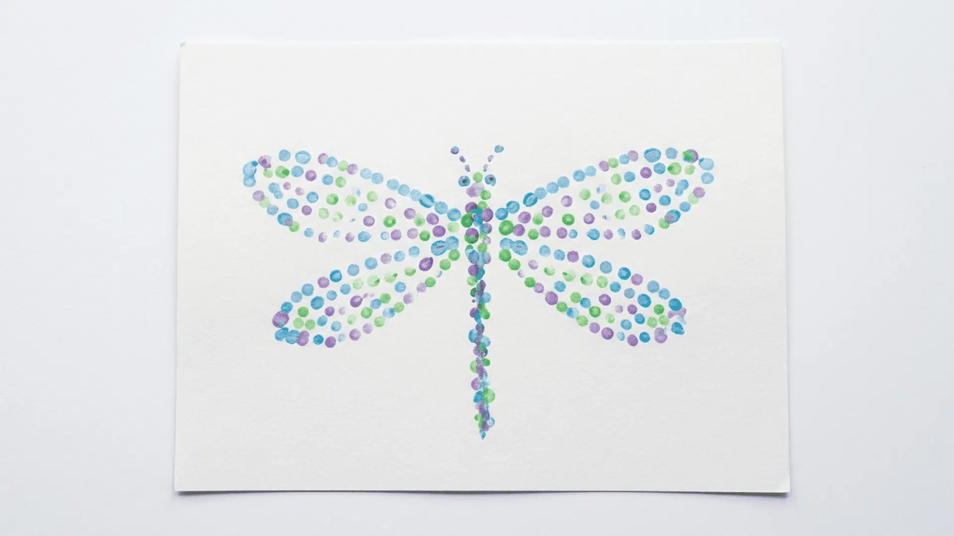 q tip dragonfly art showing a dragonfly shape built from small painted dots in blue purple and green on white paper