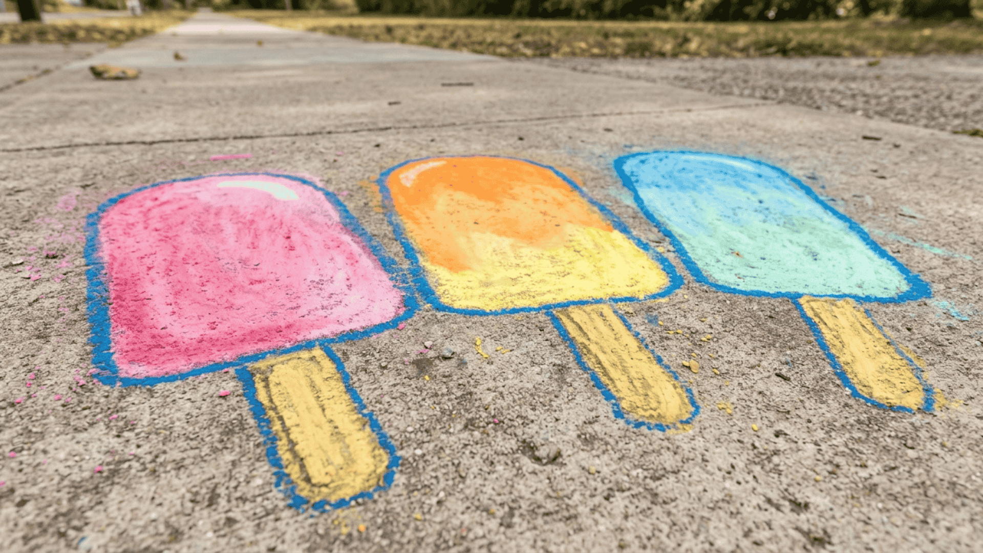sidewalk chalk ice pop mural showing three large ice pops in blended pink orange and green chalk colors on gray pavement surface