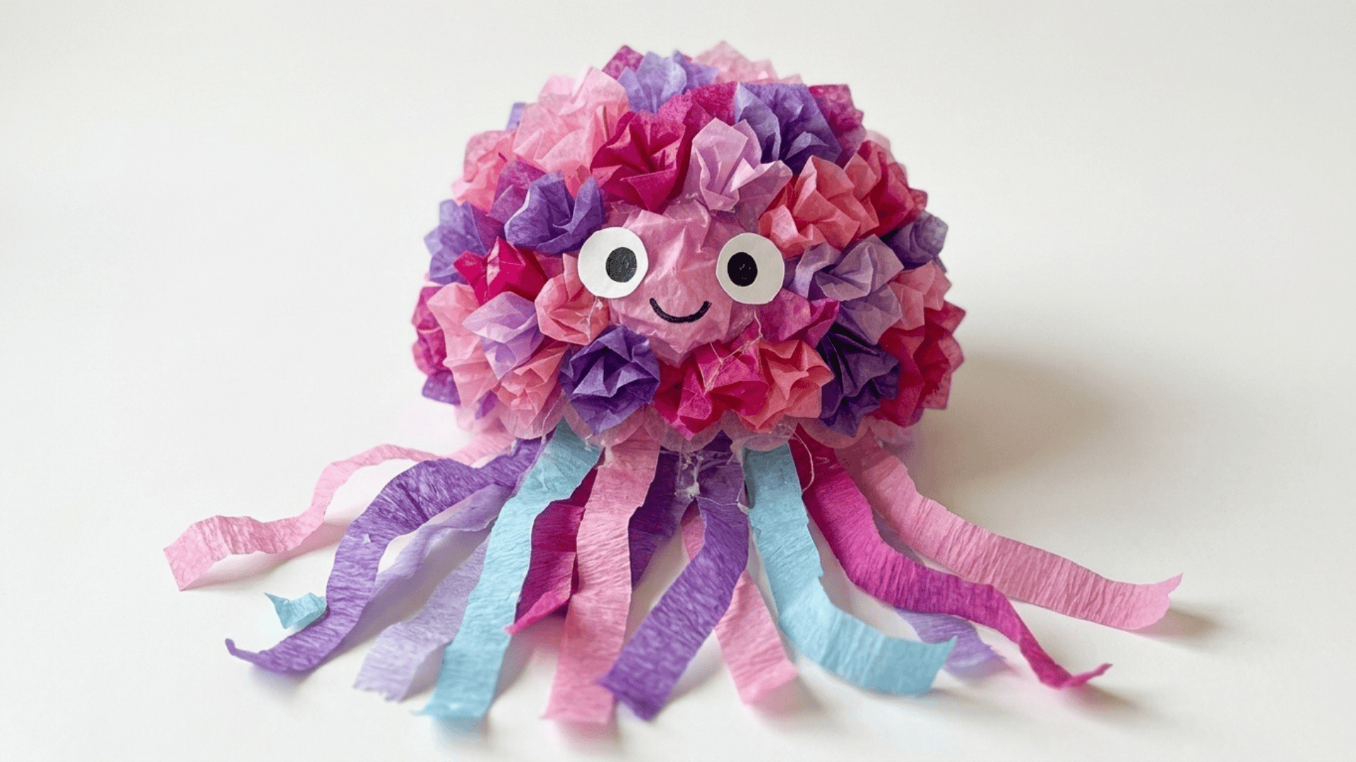tissue paper jellyfish craft showing a scrunched pink purple tissue paper dome with long crepe paper ribbon tentacles below