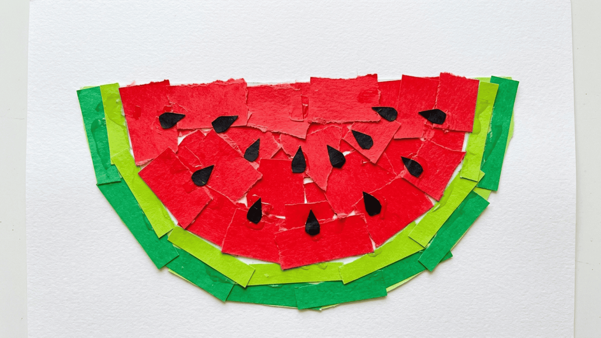 watermelon paper collage made from cut red green and black paper pieces arranged into a watermelon slice shape