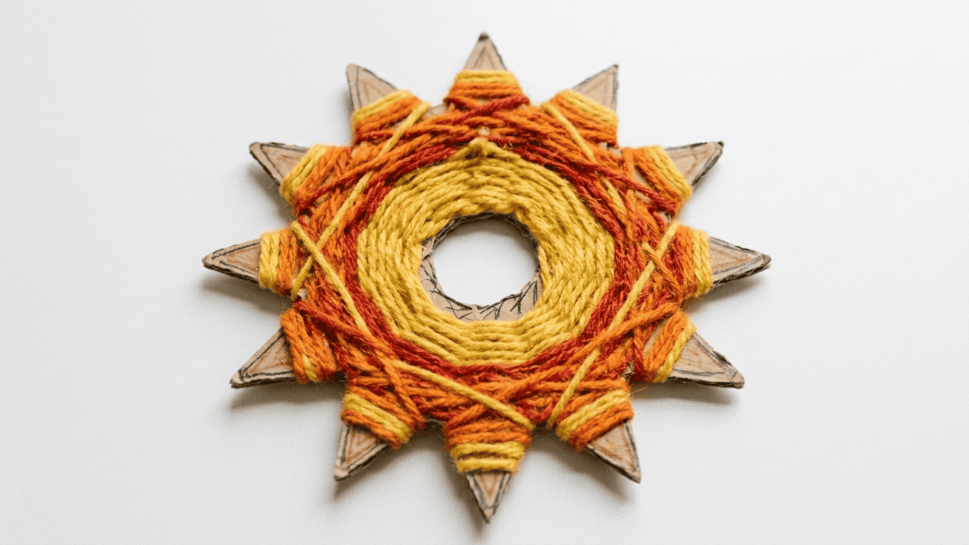 yarn sun weaving craft showing a cardboard sun shape with yellow orange and red yarn woven across the surface on white background