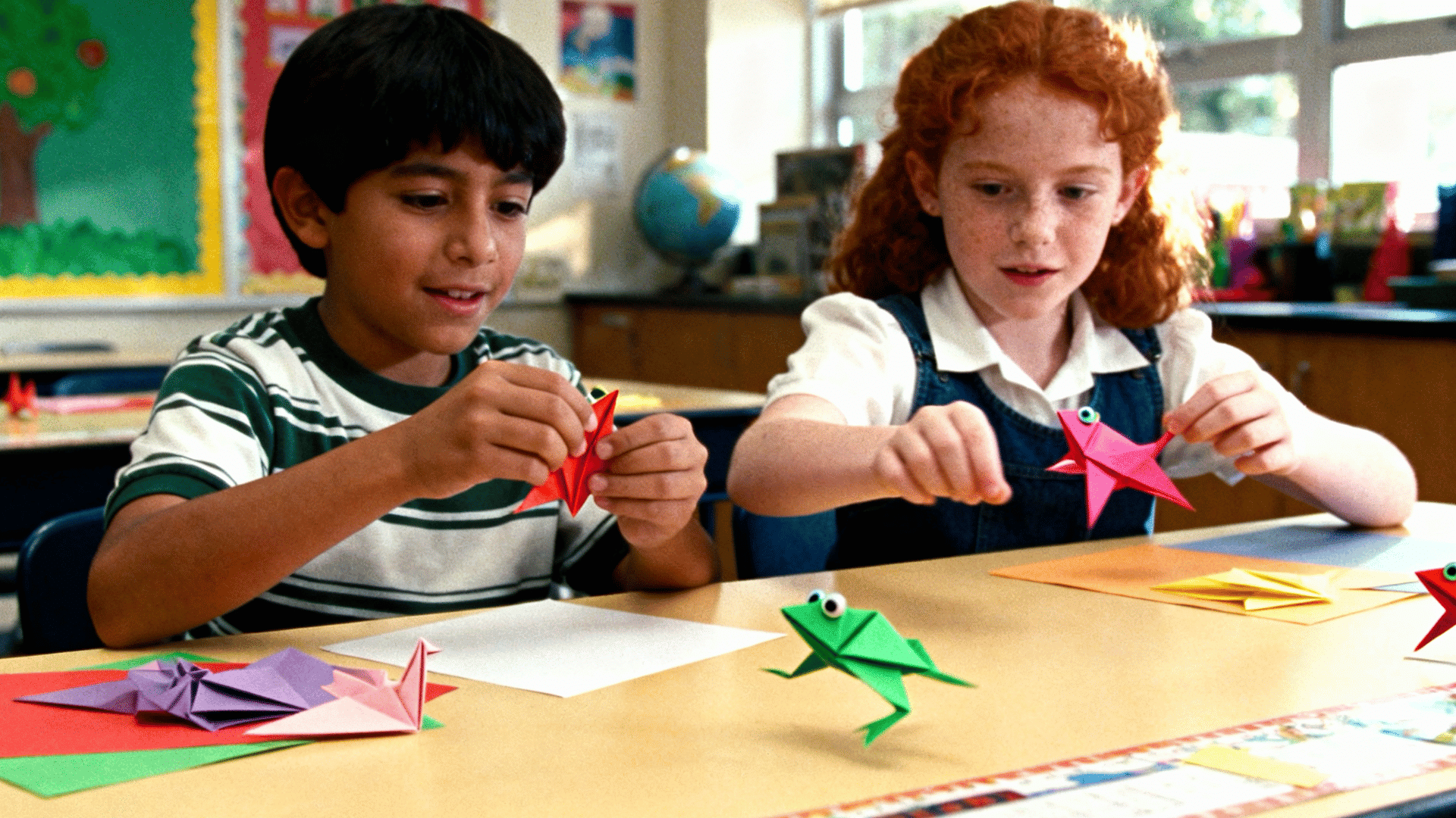 2 children folding colorful origami frogs and making them jump across a craft table, playful classroom atmosphere, bright paper designs, realistic photography, 169 aspect ratio