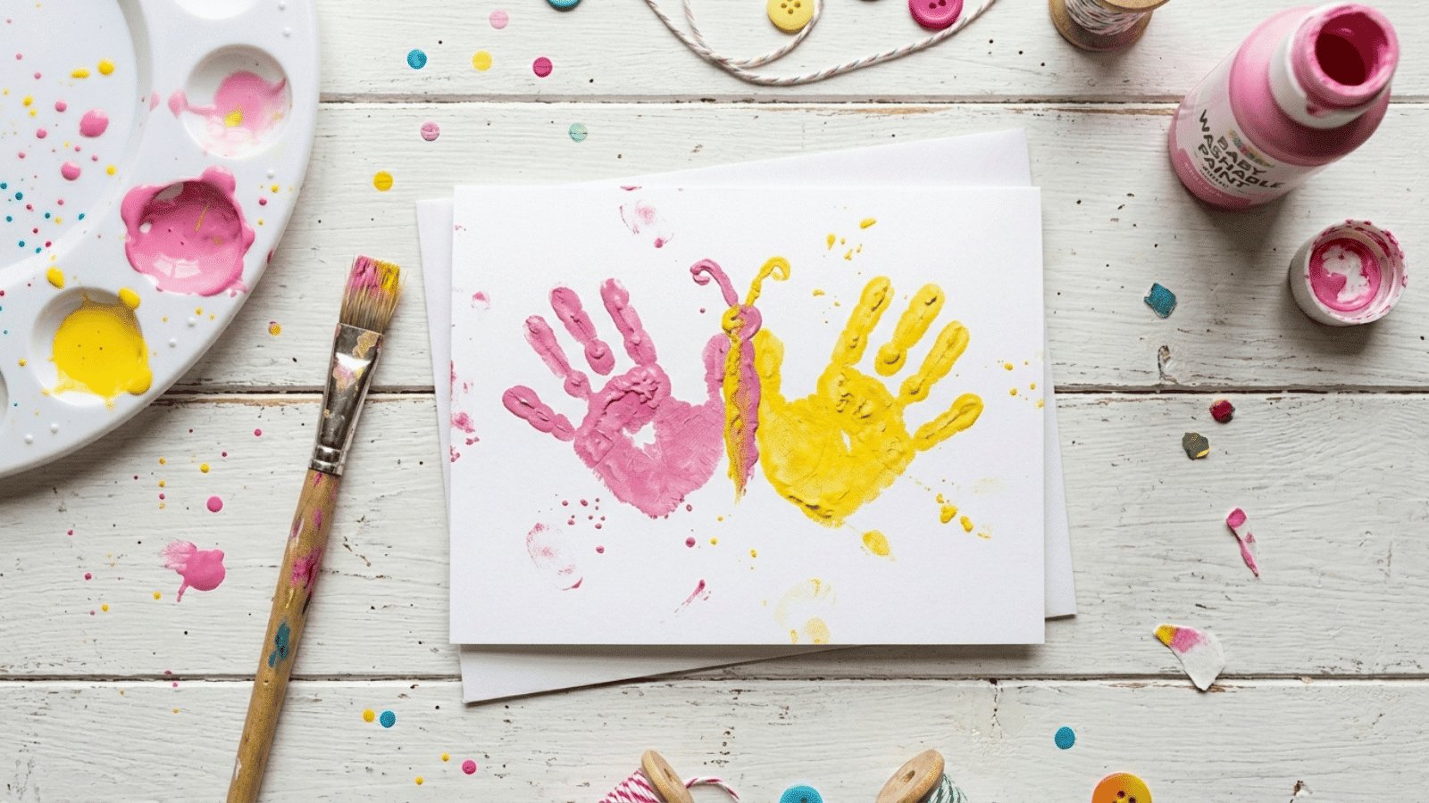 diy Mother’s Day card with colorful handprints and paint supplies on a white wooden table, perfect for kids’ craft ideas