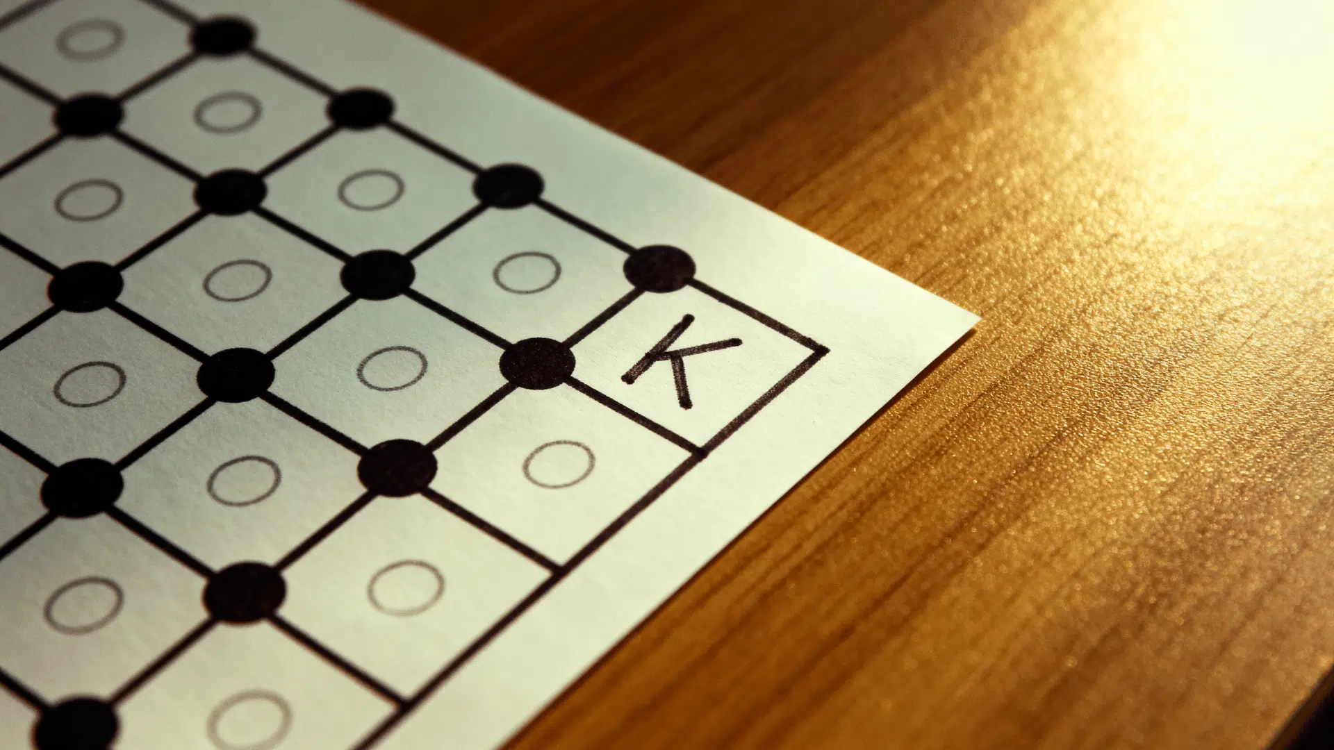 Dots and Boxes paper game with connected dots and a completed box marked with the letter K.