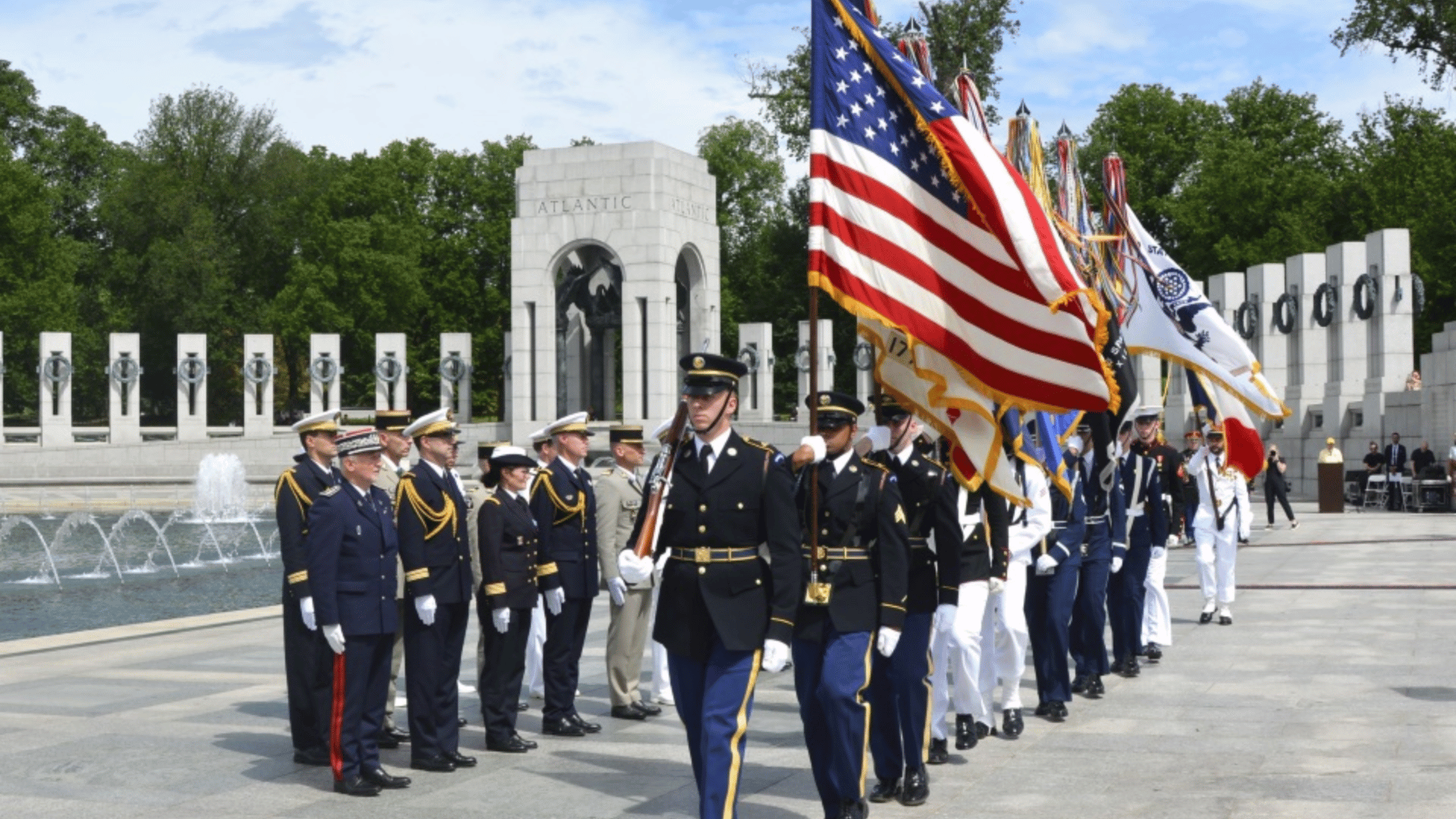 military honor guard marches with American flags at a national memorial during a formal remembrance ceremony for veterans