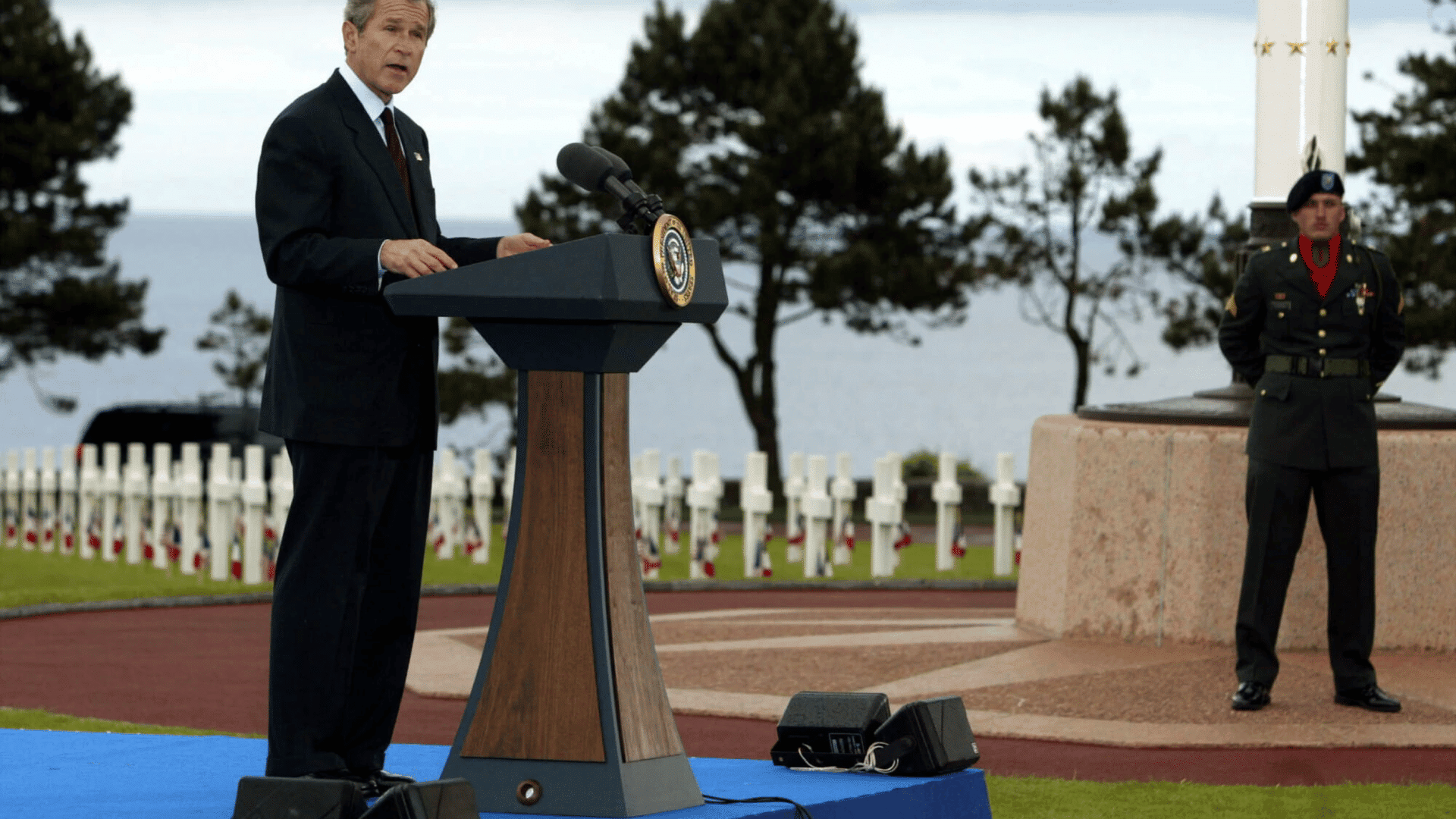 president speaks at a military cemetery memorial ceremony, honoring fallen service members beside rows of white grave markers.