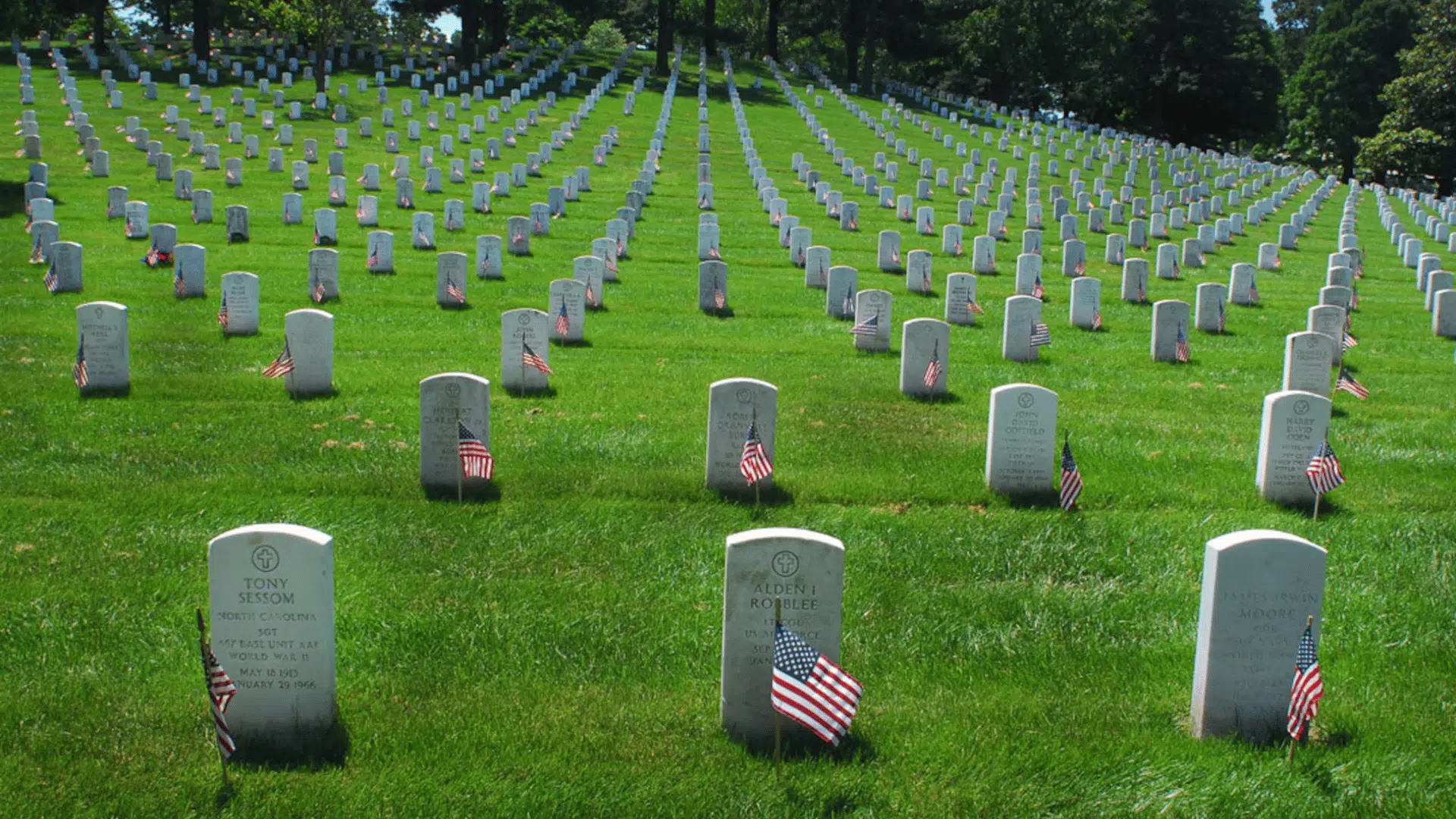rows of white headstones with American flags line a peaceful military cemetery in tribute to fallen U.S. service members.