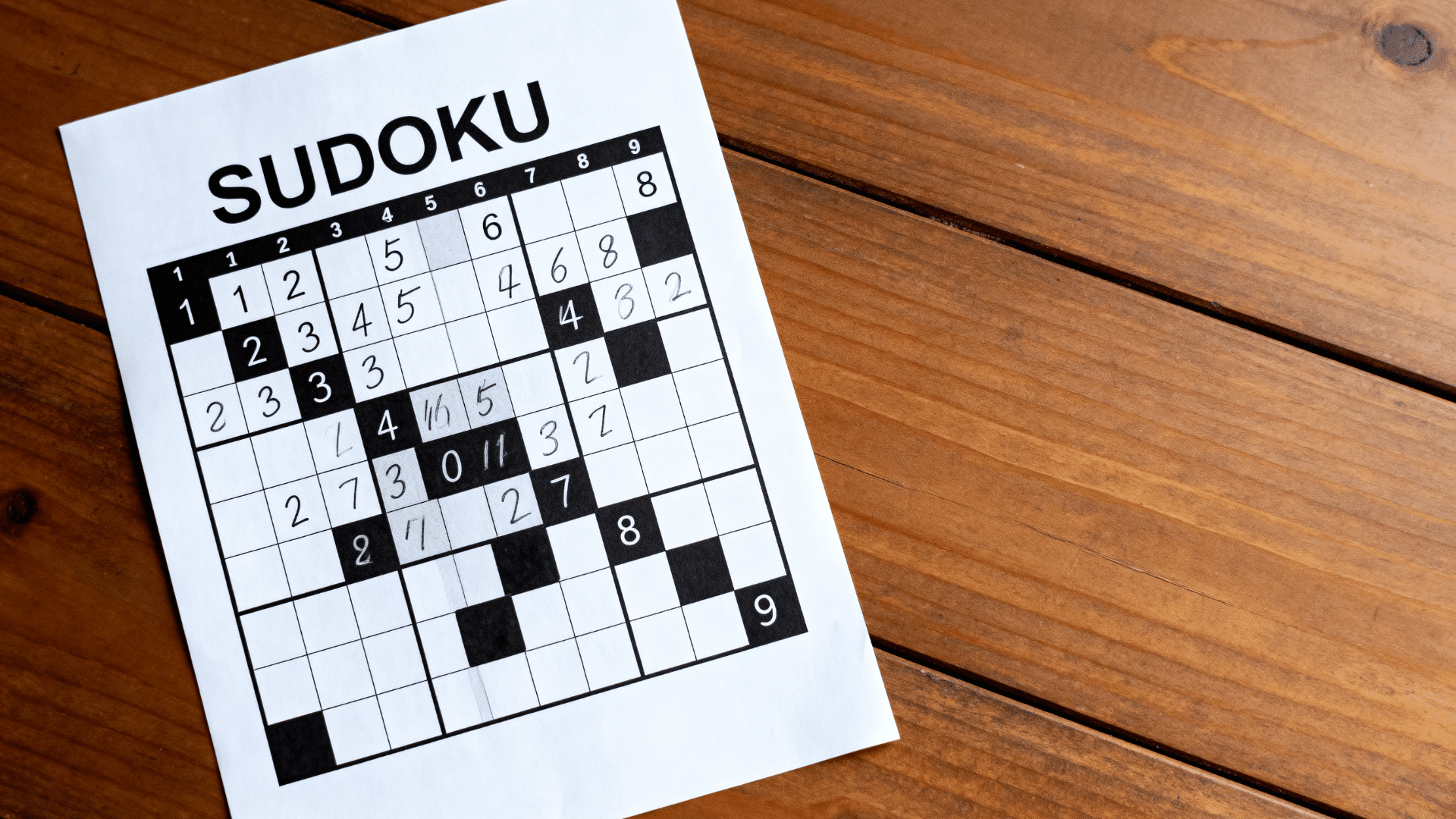 Sudoku puzzle sheet with partially filled number grid placed on a wooden table.