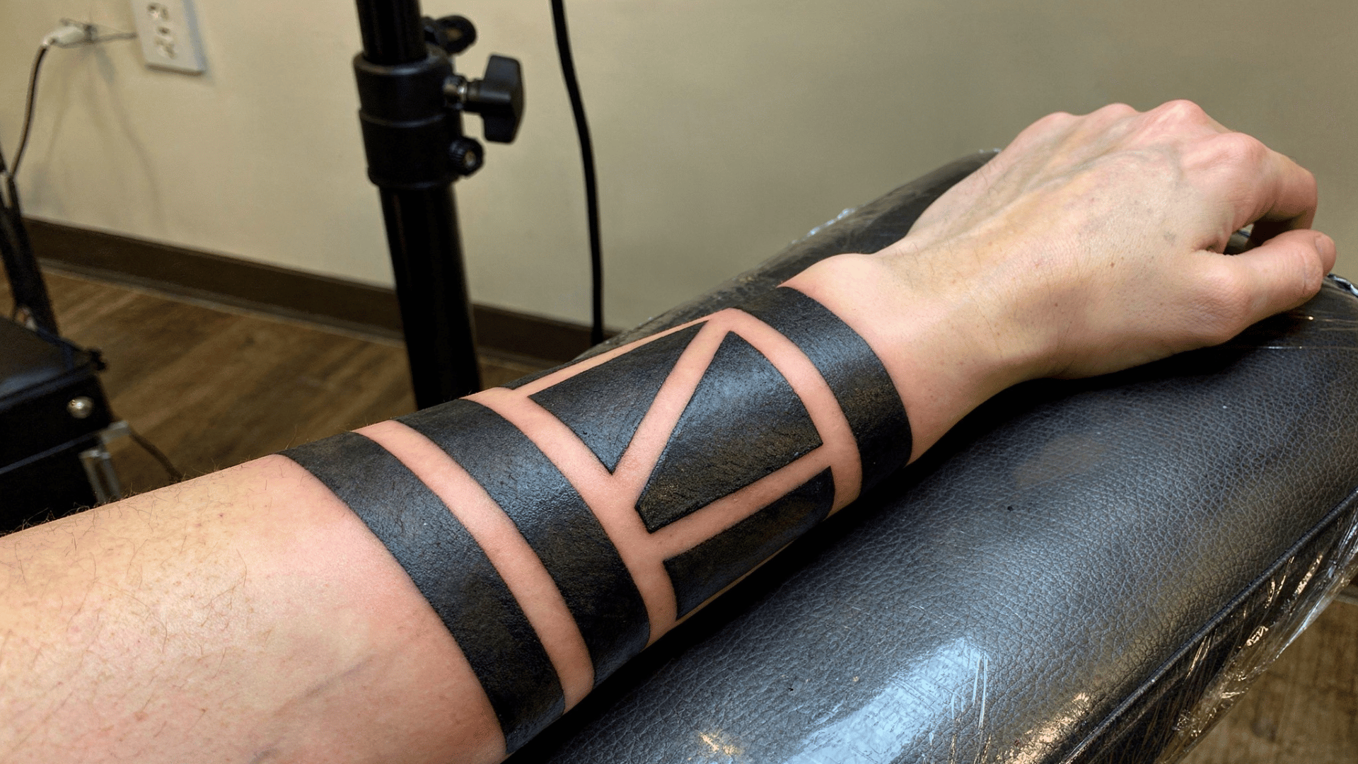 close-up of a blackwork tattoo with bold geometric patterns and solid black ink being tattooed on a person's forearm