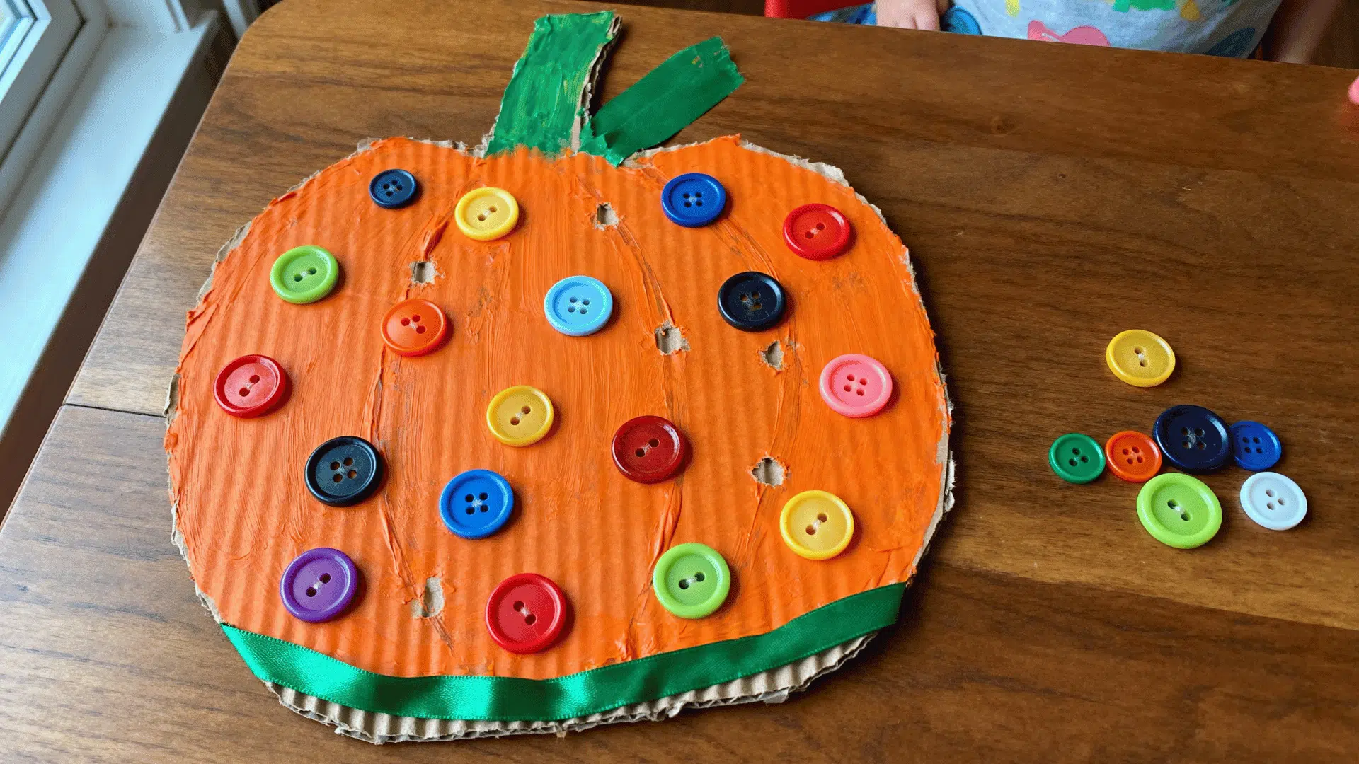 button-decorated pumpkin craft covered with colorful buttons and green trim