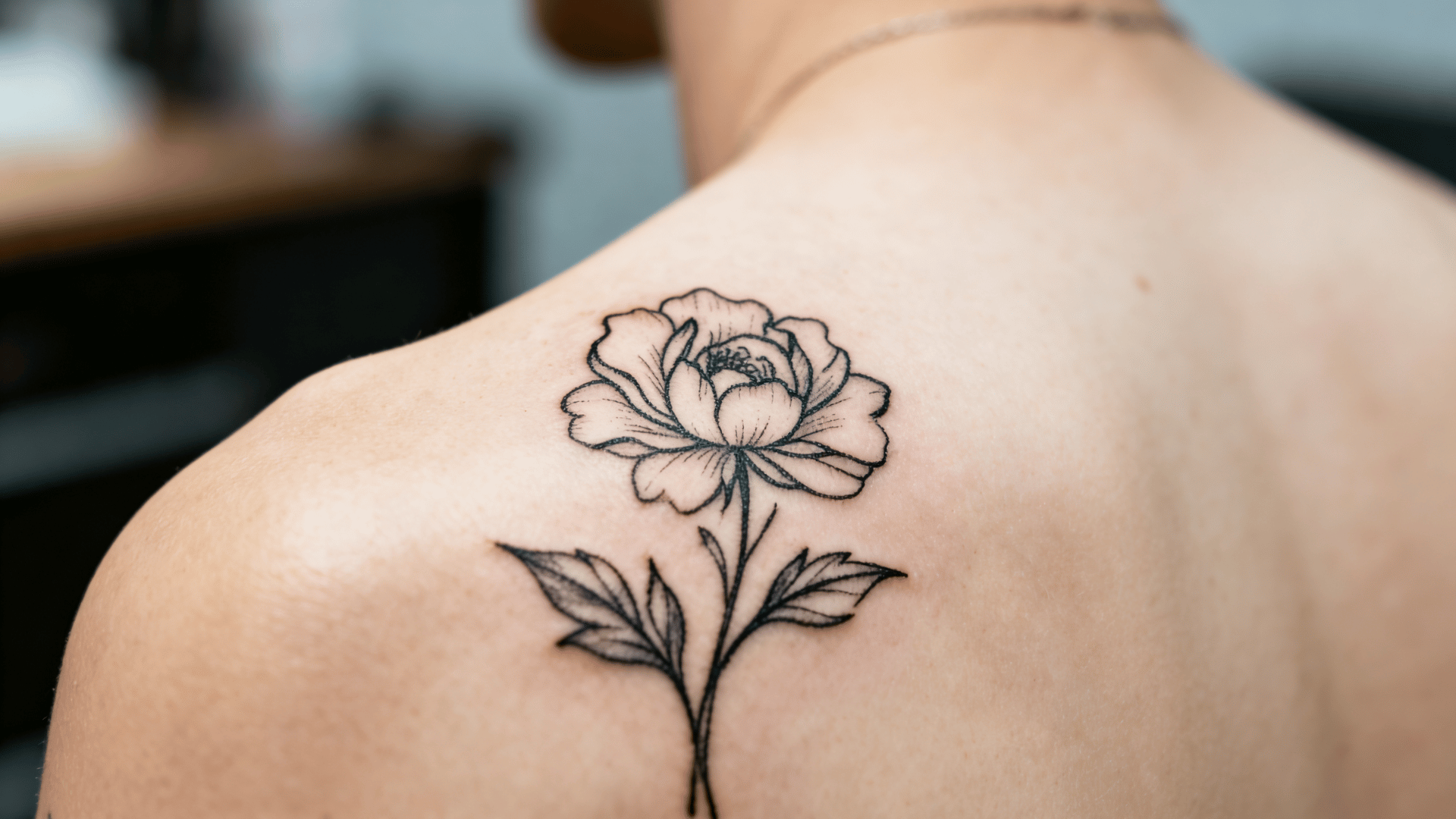 fine-line floral tattoo with delicate details being tattooed on a person's shoulder during a professional tattoo session.