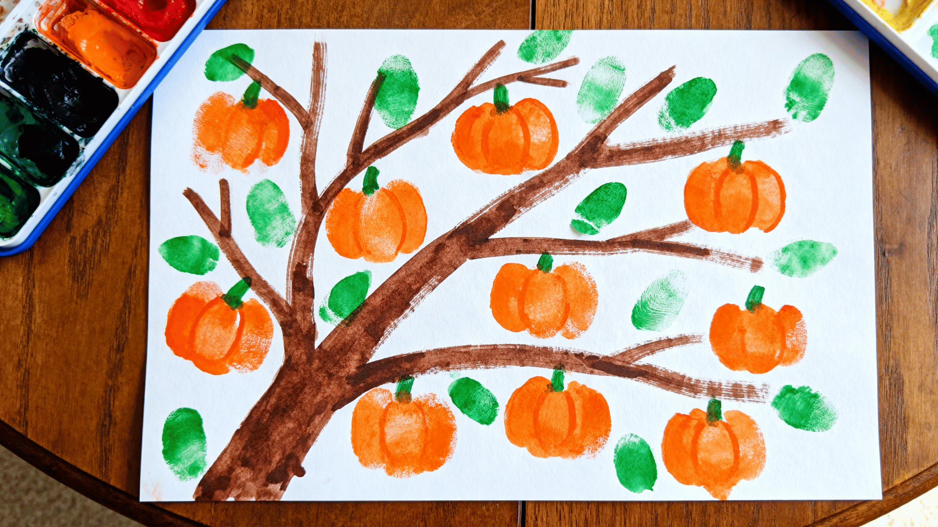 fingerprint tree art featuring orange pumpkin prints and green leaves made by a toddler