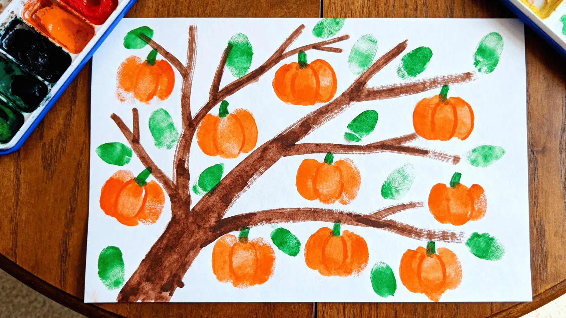 fingerprint tree art featuring orange pumpkin prints and green leaves made by a toddler