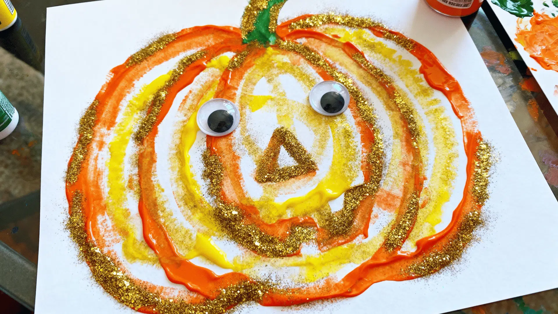 glitter glue pumpkin art decorated with colorful glitter lines and googly eyes