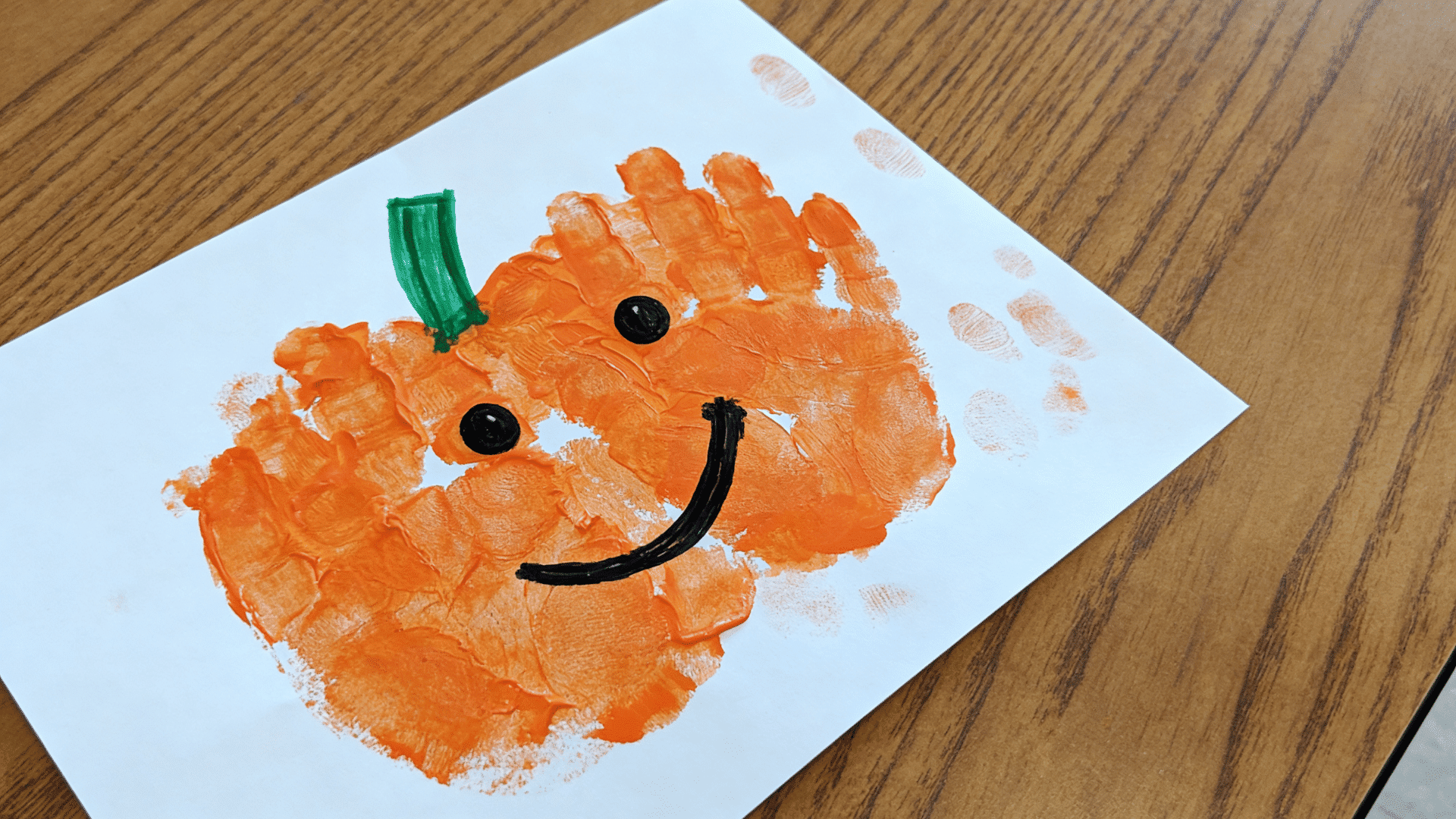 toddler-made handprint pumpkin craft painted with orange paint on white cardstock.