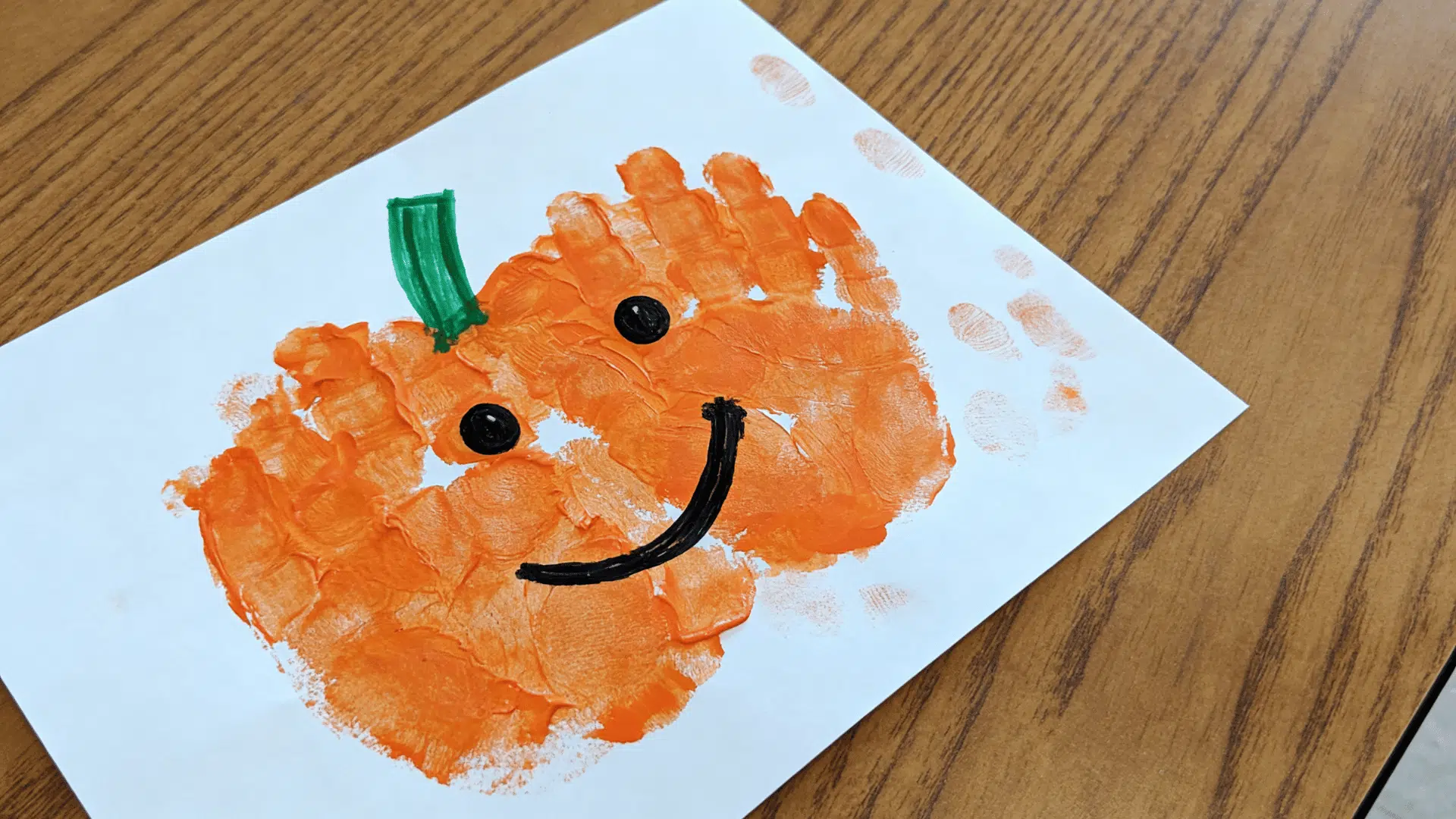 toddler-made handprint pumpkin craft painted with orange paint on white cardstock.