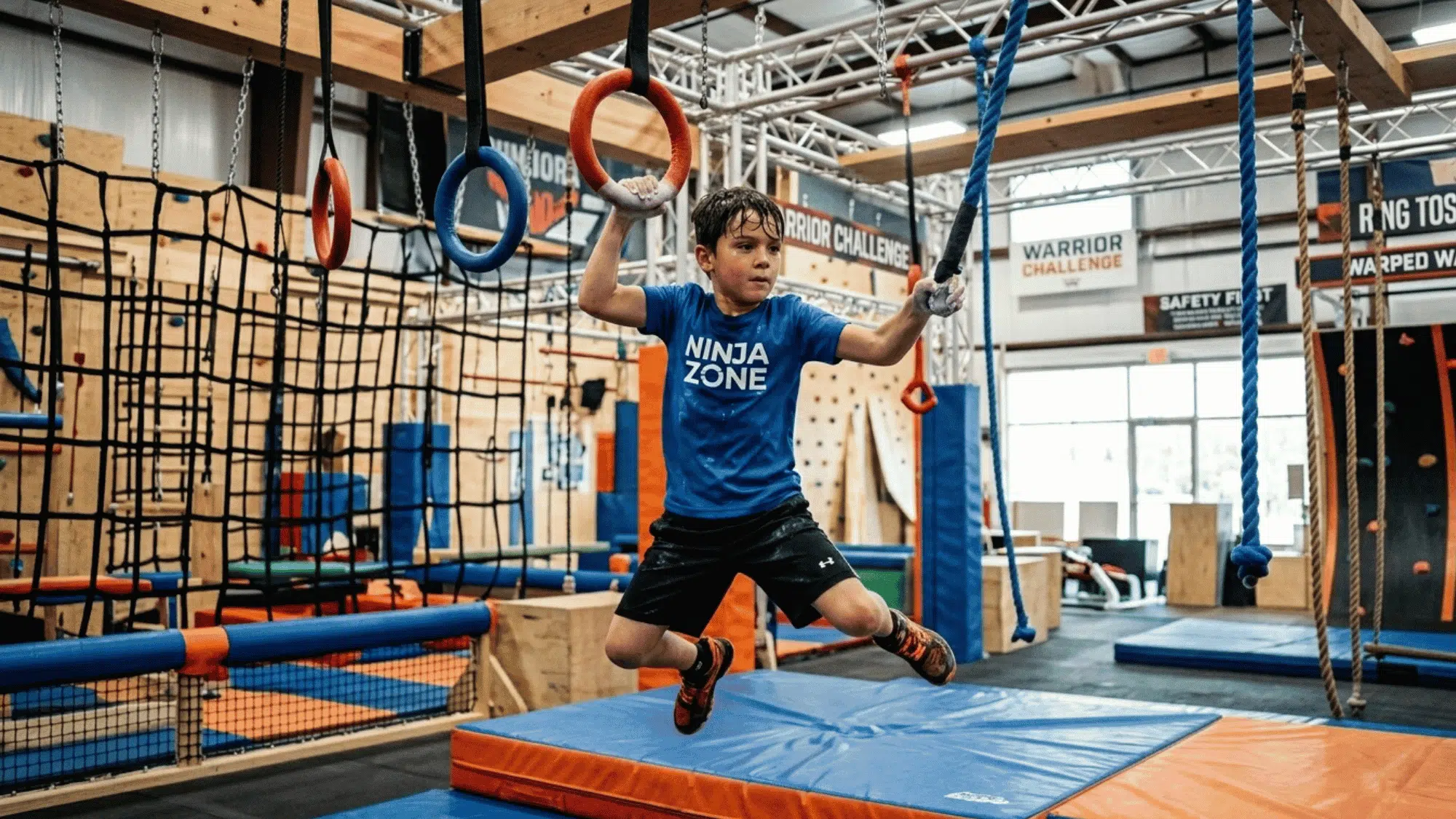 child swings between rings on a ninja warrior obstacle course inside a training gym.