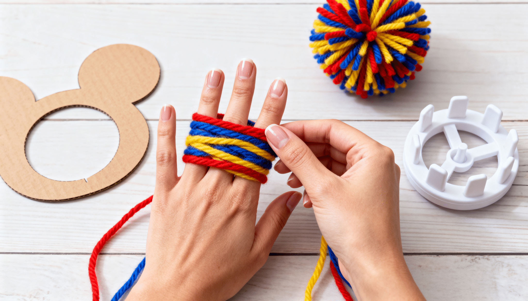 Hands wrapping colorful yarn around fingers to start making a pom pom.