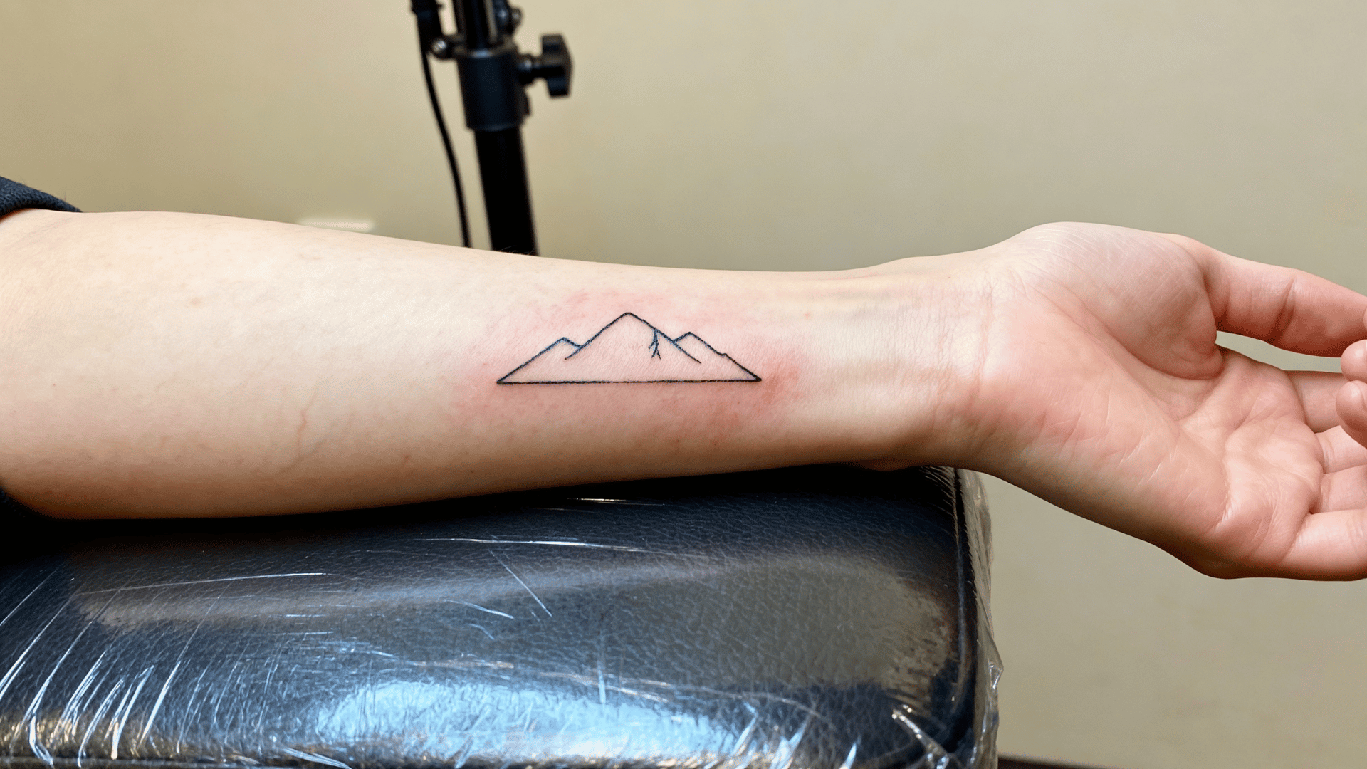 small minimalist mountain tattoo with clean lines being inked on a person's wrist in a professional tattoo studio