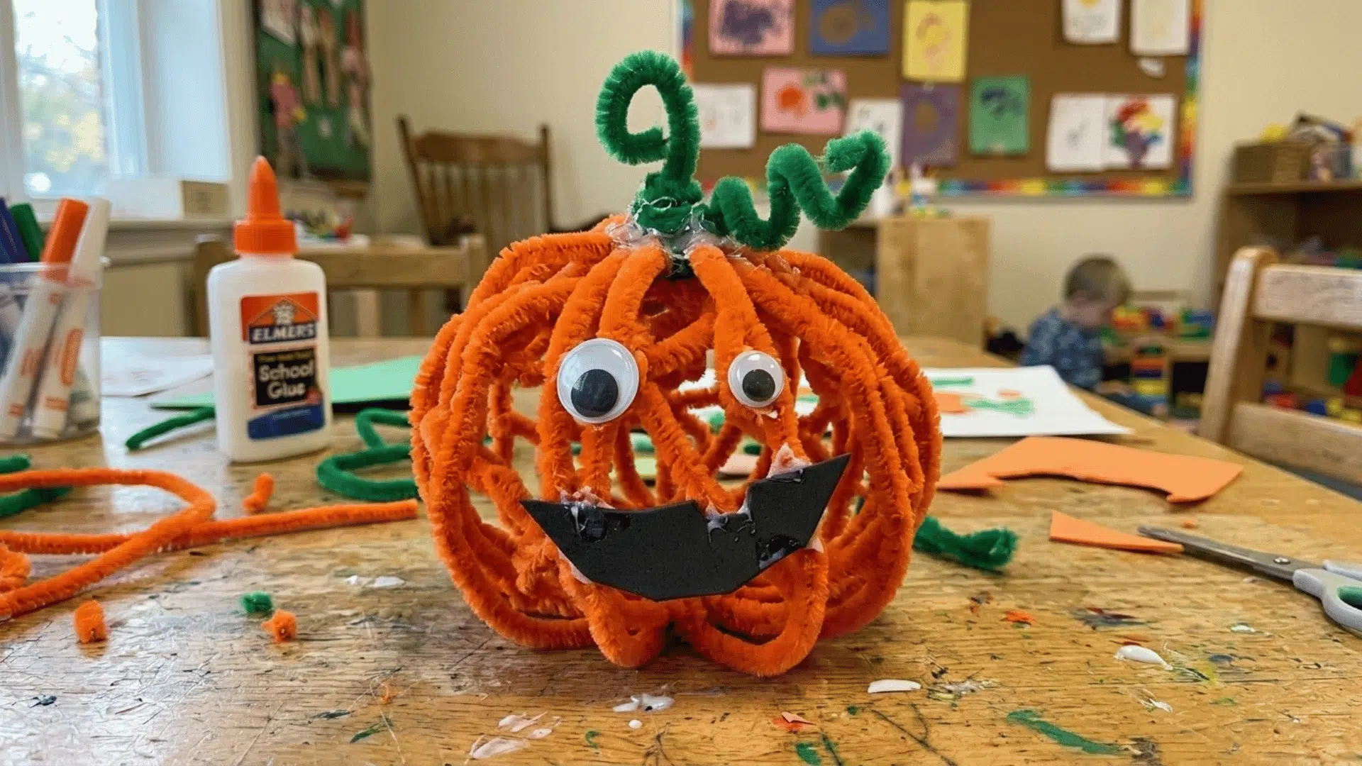 pumpkin craft made from orange pipe cleaners with googly eyes and a green stem.