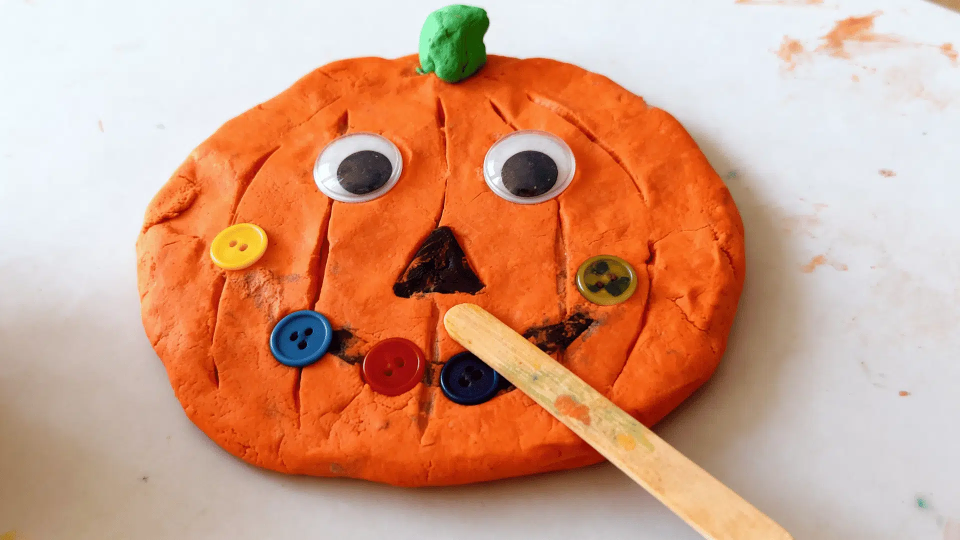 play-doh pumpkin face decorated with googly eyes and colorful buttons