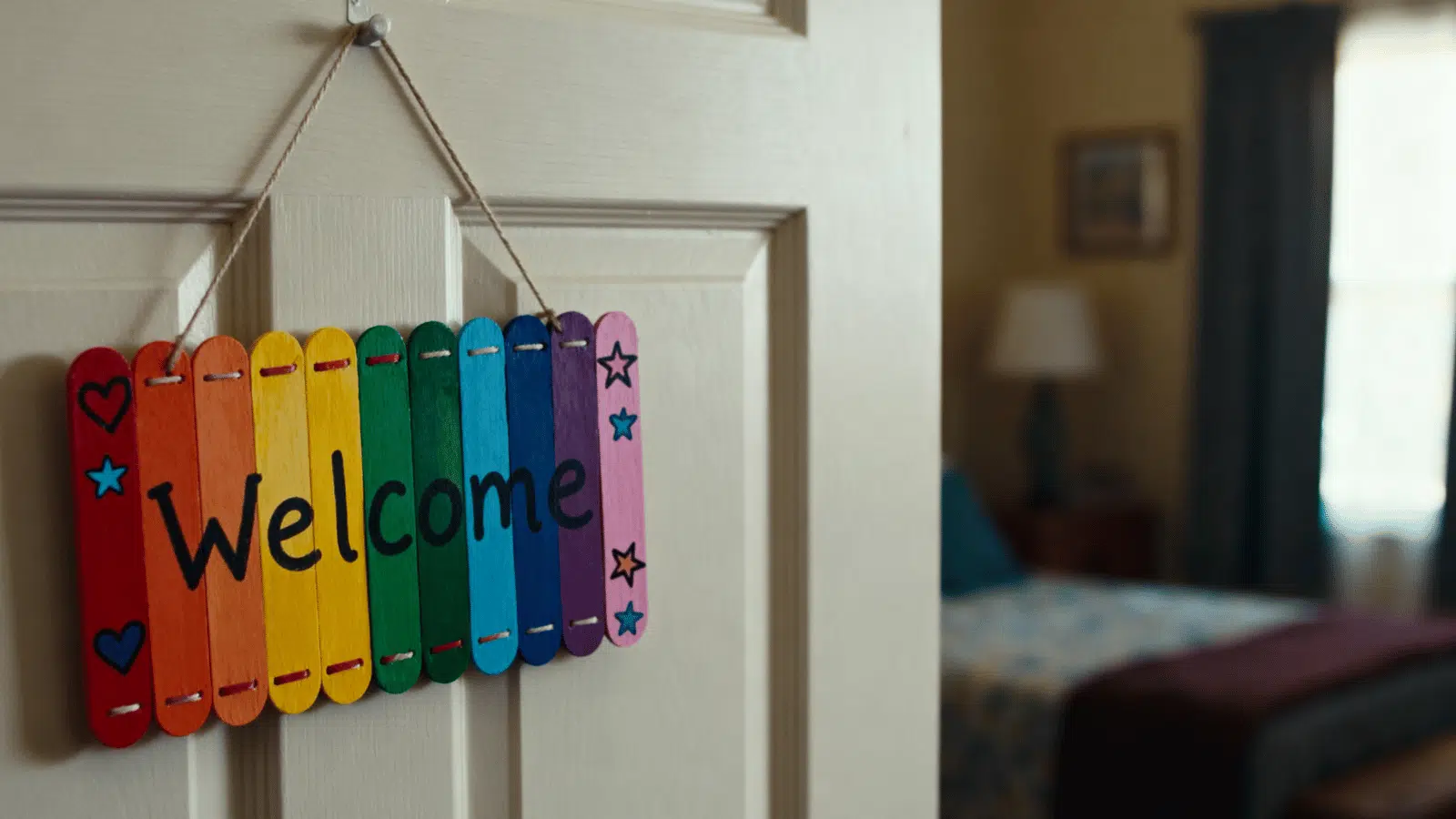 handmade popsicle stick door hanger with bright paint and small star details hanging on a room door.