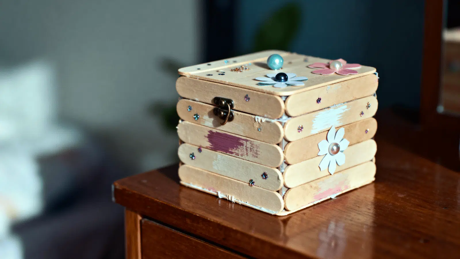 handmade popsicle stick jewelry box with a lid and bead details placed on a dresser.