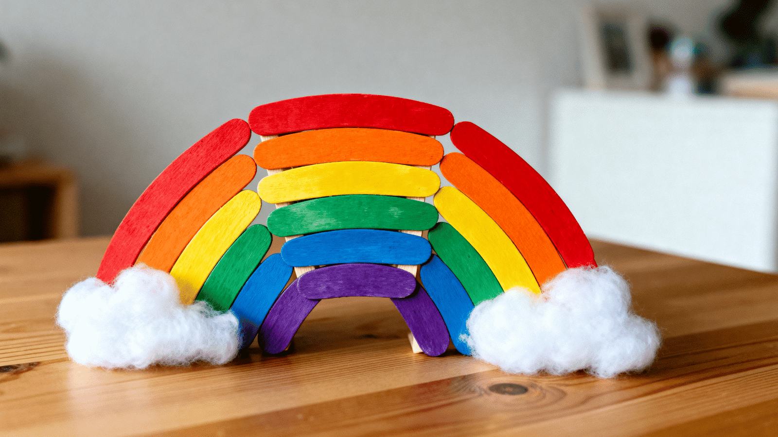 handmade popsicle stick rainbow with painted colors and cotton clouds displayed on a shelf.