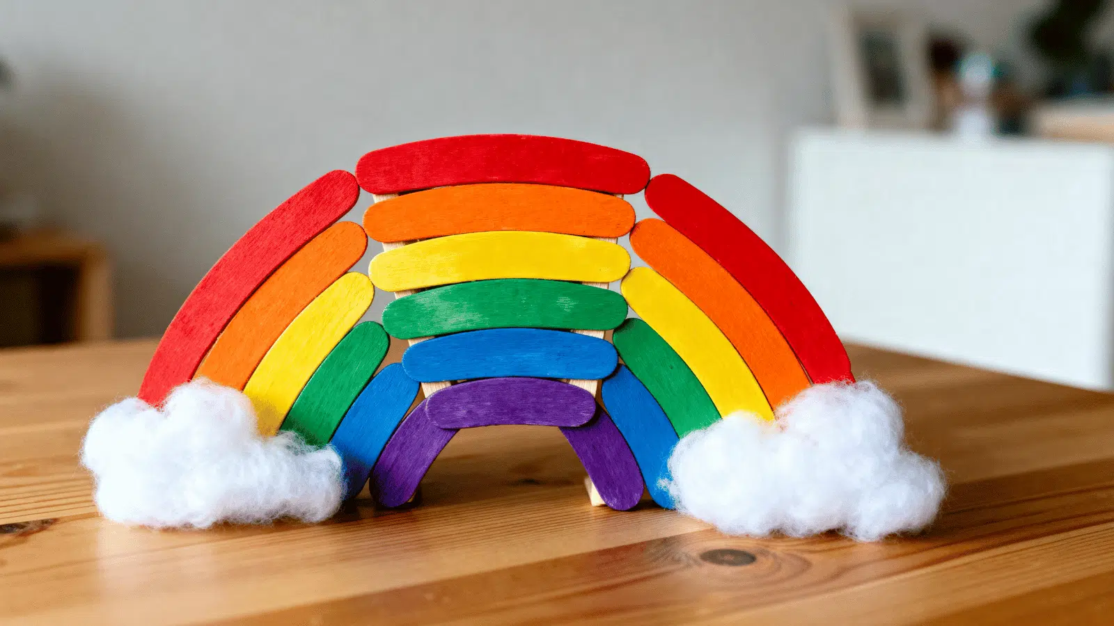 handmade popsicle stick rainbow with painted colors and cotton clouds displayed on a shelf.