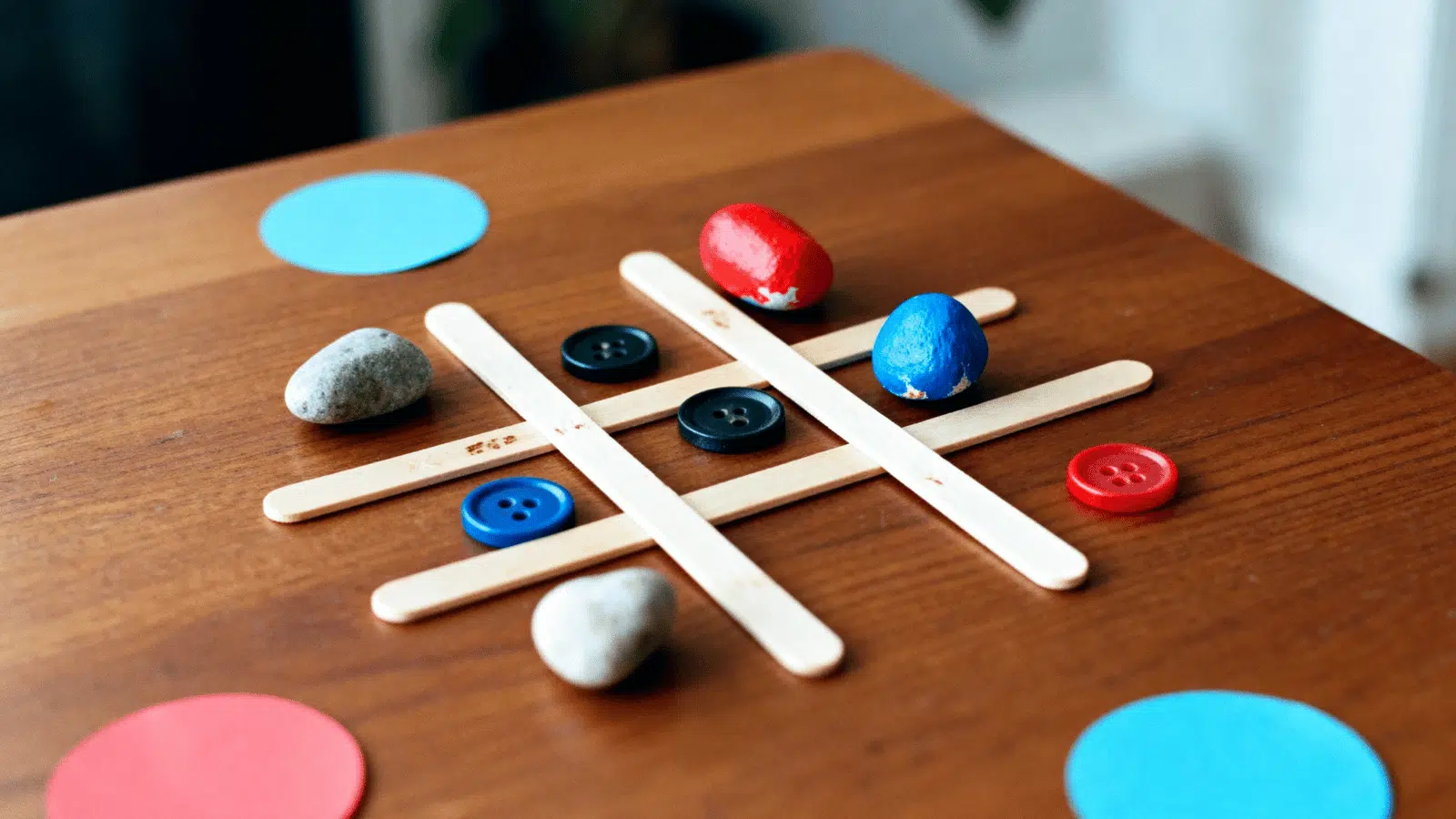 handmade popsicle stick tic-tac-toe game with colorful pieces arranged on a table.