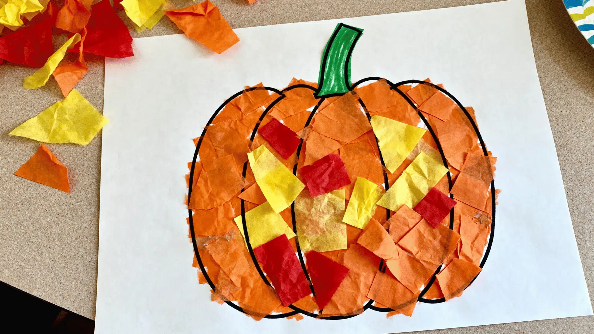 pumpkin tissue paper collage made by a toddler using colorful torn tissue paper pieces.