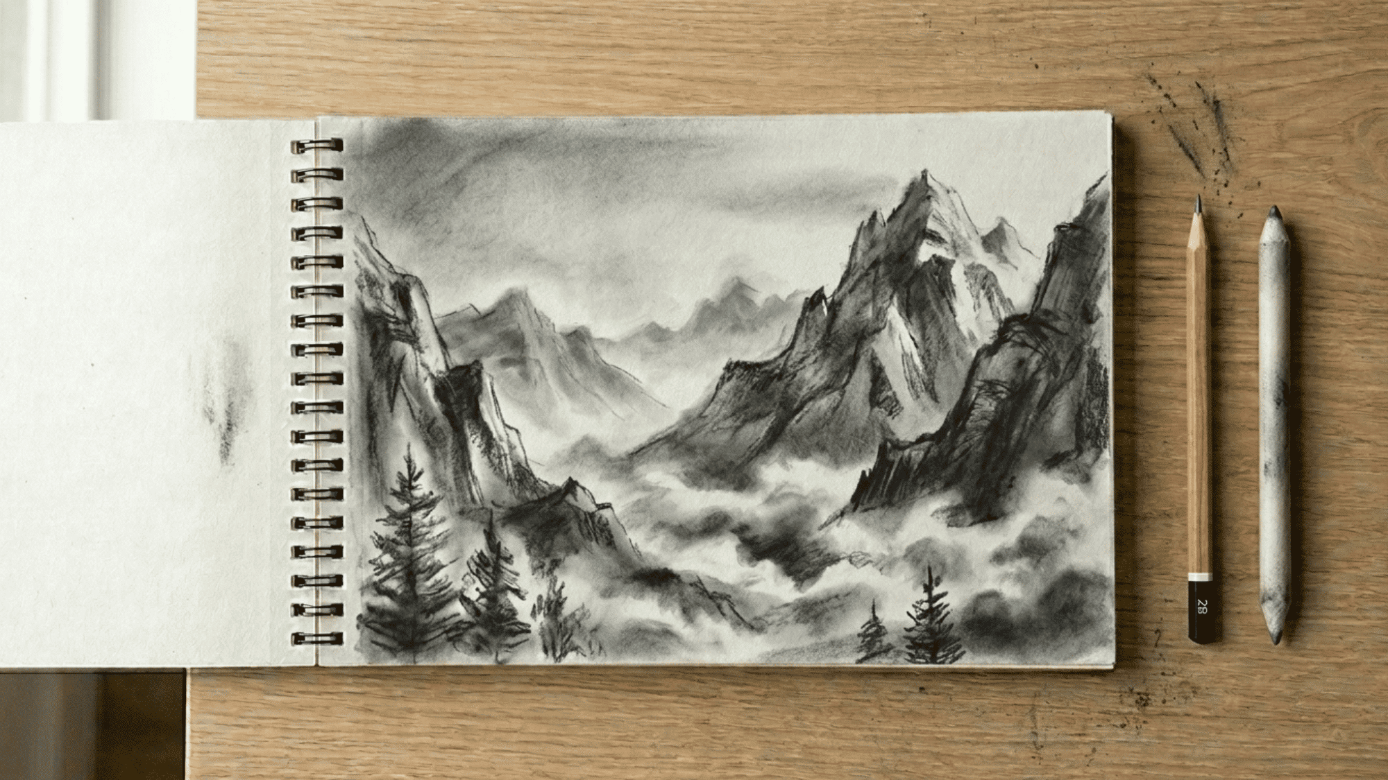 sketchbook on artist desk showing smudged shading in a mountain scene