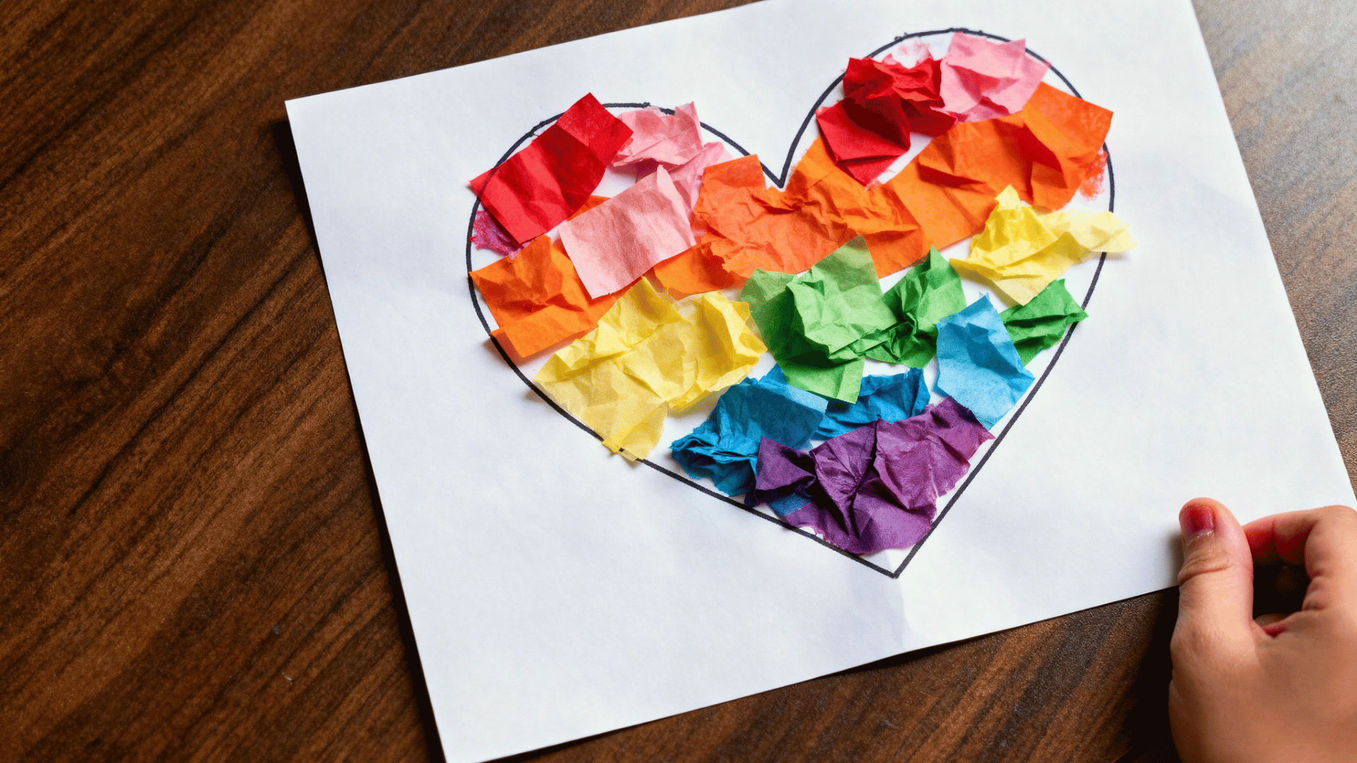 tissue paper heart craft made by a toddler using colorful torn paper pieces.
