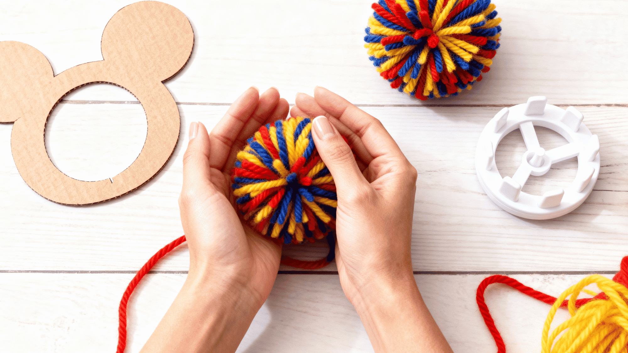 Hands fluffing a finished yarn pom pom to make it soft and round.