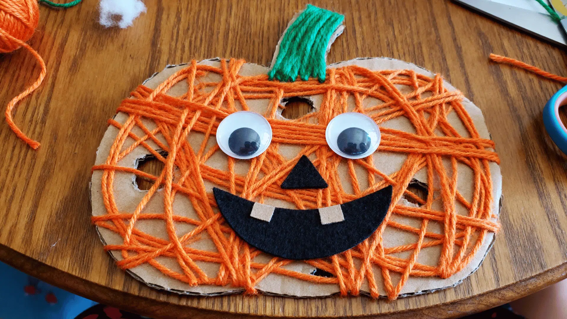 yarn-wrapped pumpkin craft decorated with googly eyes and a felt smile