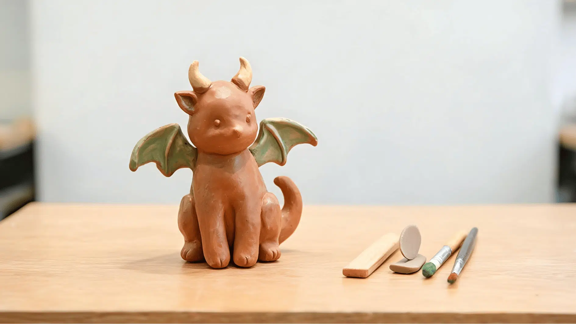hand sculpted clay fantasy creature with wings horns and simple modeling tools nearby