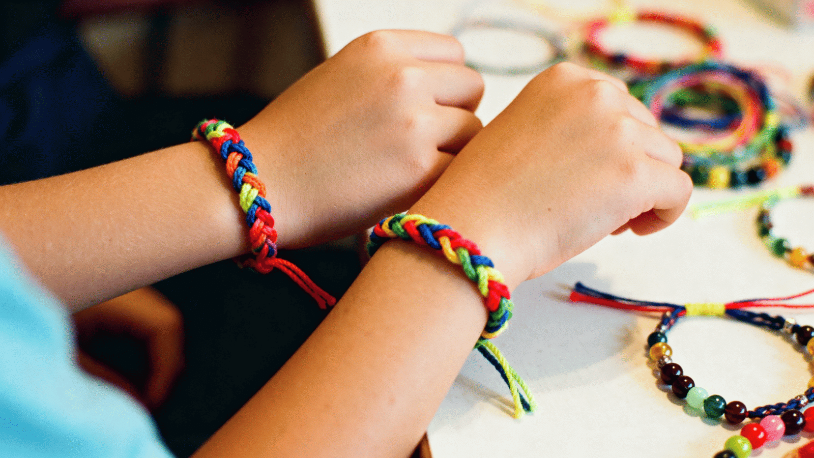 two kids wearing colorful DIY friendship bracelets made at home, easy and fun simple craft for kids ages 6 to 12