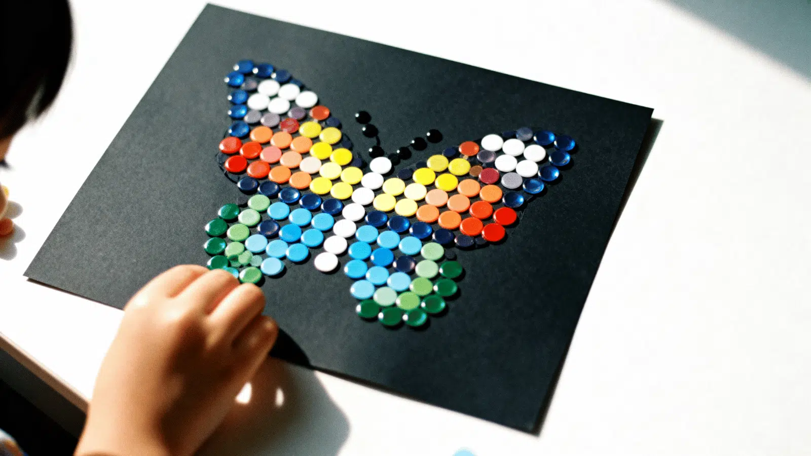 a sticker mosaic butterfly made with colorful dot stickers on black paper by kids, a simple craft for ages 6 to 12